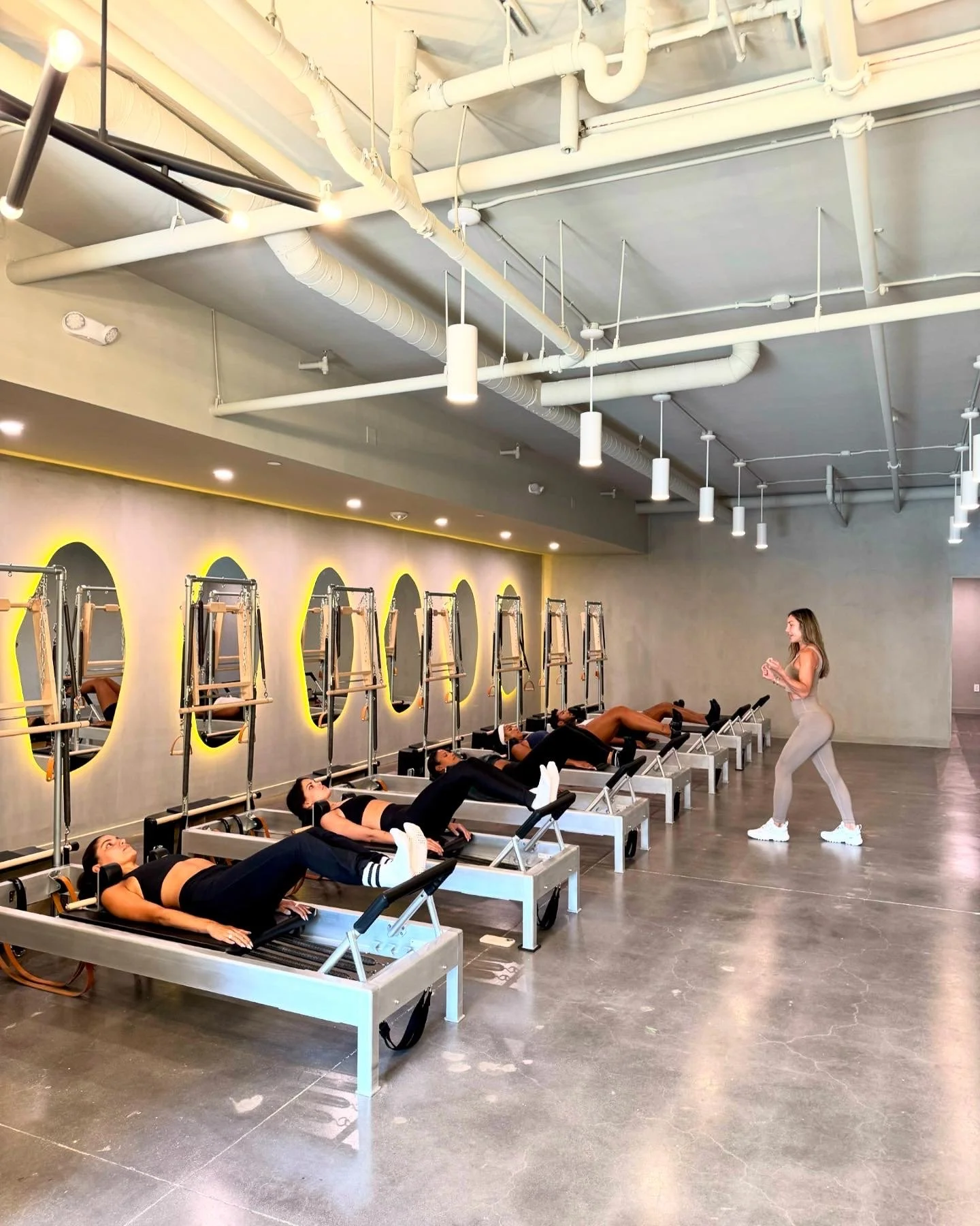 Women in a fitness studio on Pilates reformer machines with an instructor.