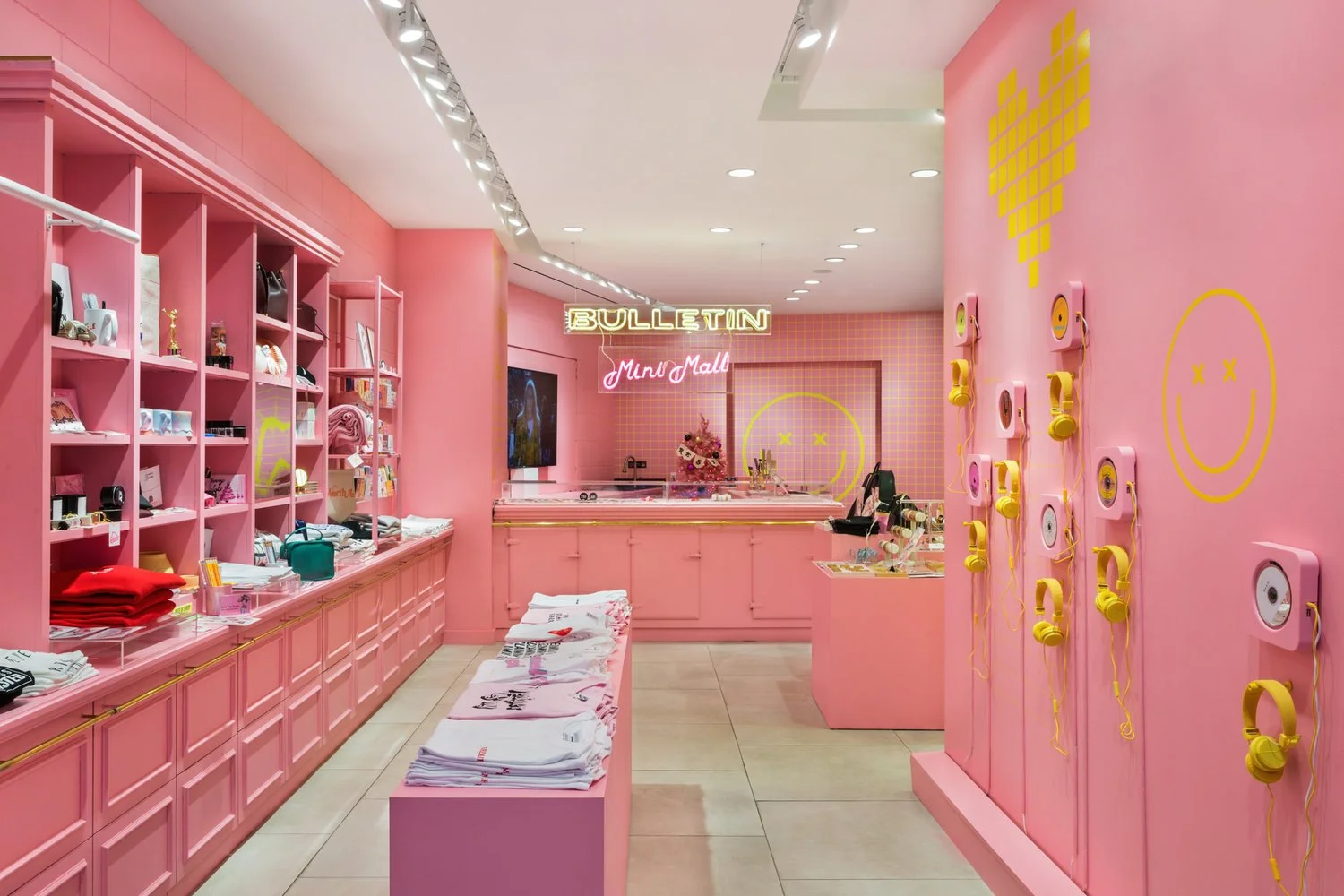 Pink-themed store interior with shelves displaying merchandise, a table with folded clothes, yellow smiley face graphics, and wall-mounted headphones.