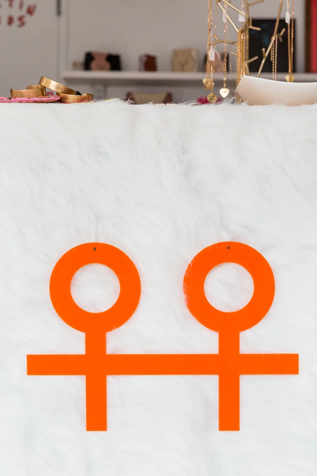 Orange double Venus symbols on white furry background, with jewelry and accessories in the background.