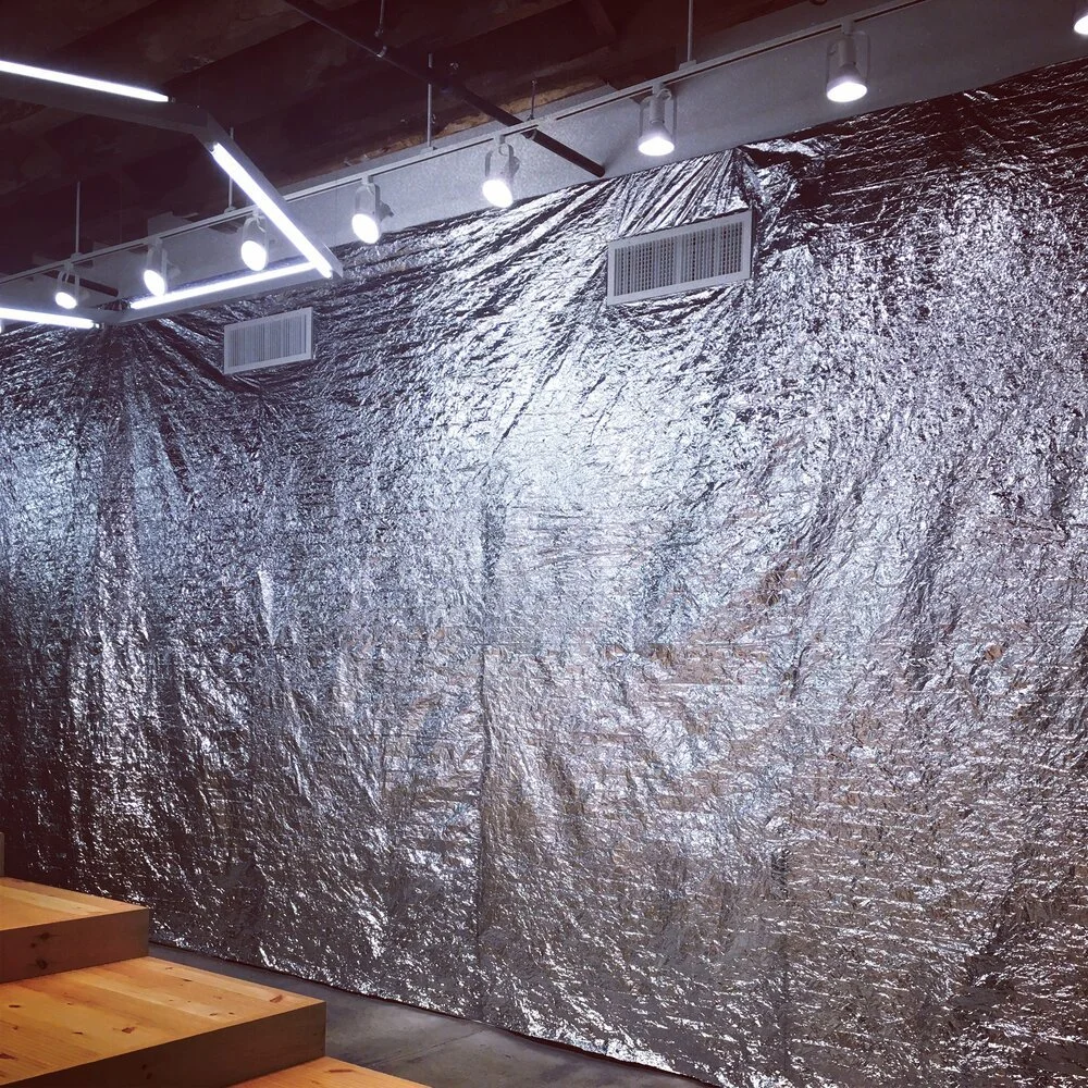 Room with a wall covered in silver foil insulation, overhead white LED strip lights and spotlights, wooden steps in the foreground.