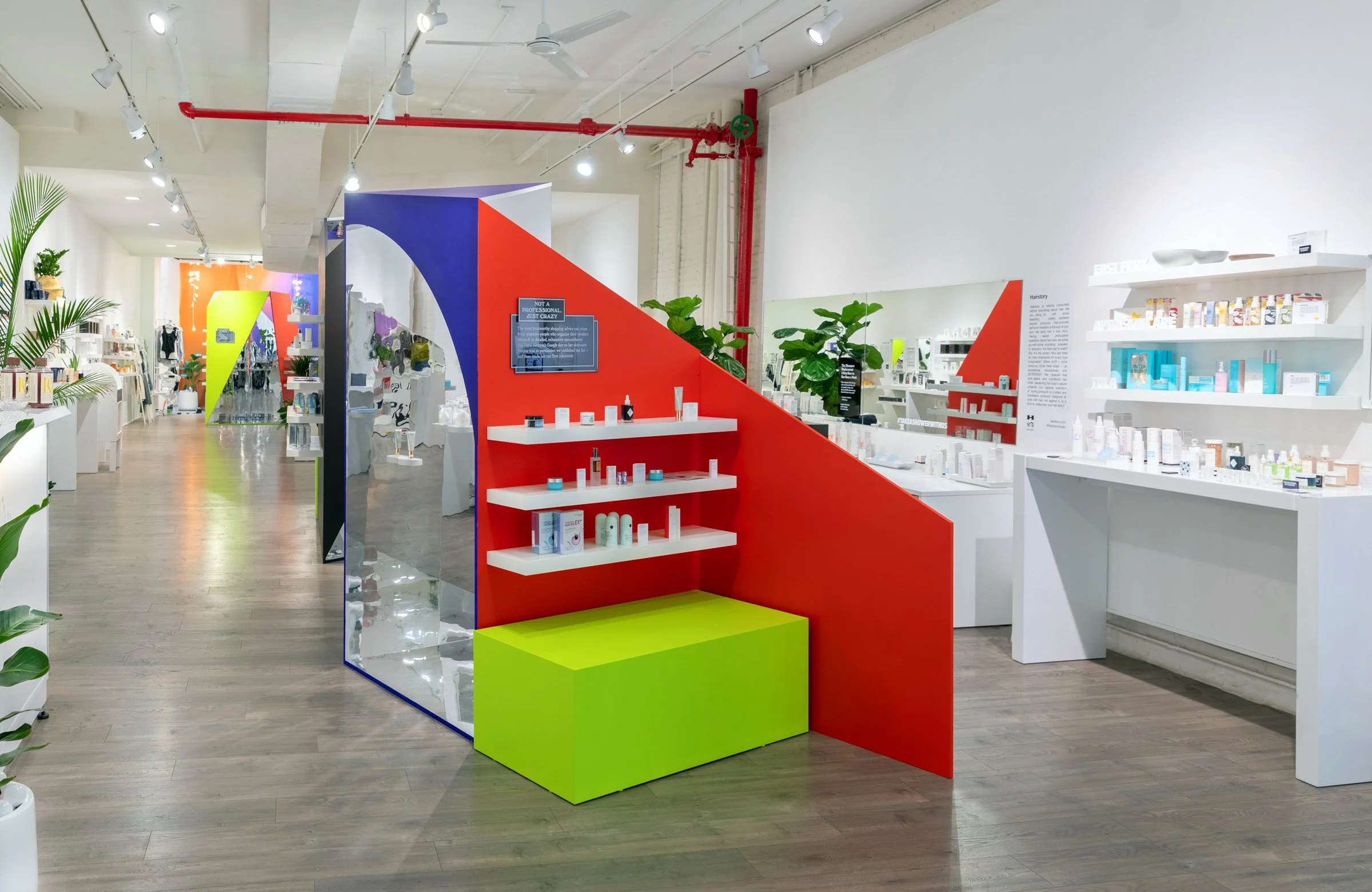 Interior of a modern retail store with colorful displays and shelves containing various beauty and skincare products. Bright colors like red, green, and blue are featured prominently in the design. The space has a clean, minimalistic aesthetic with wooden flooring and white walls. Potted plants add a touch of greenery.