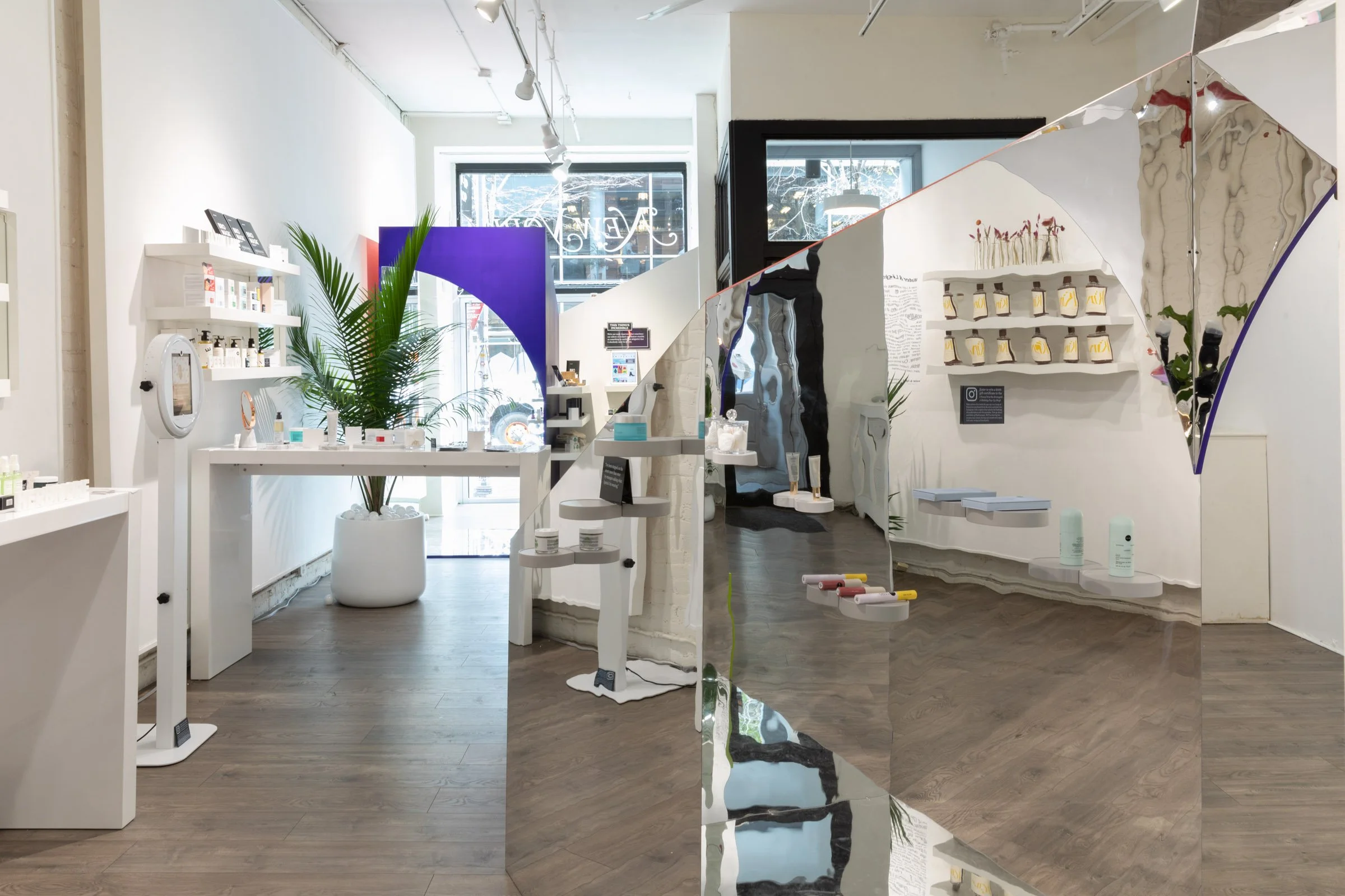 Interior of a modern retail store with white shelves displaying skincare and beauty products, decorative plants, mirrors, and a hexagonal floor pattern.