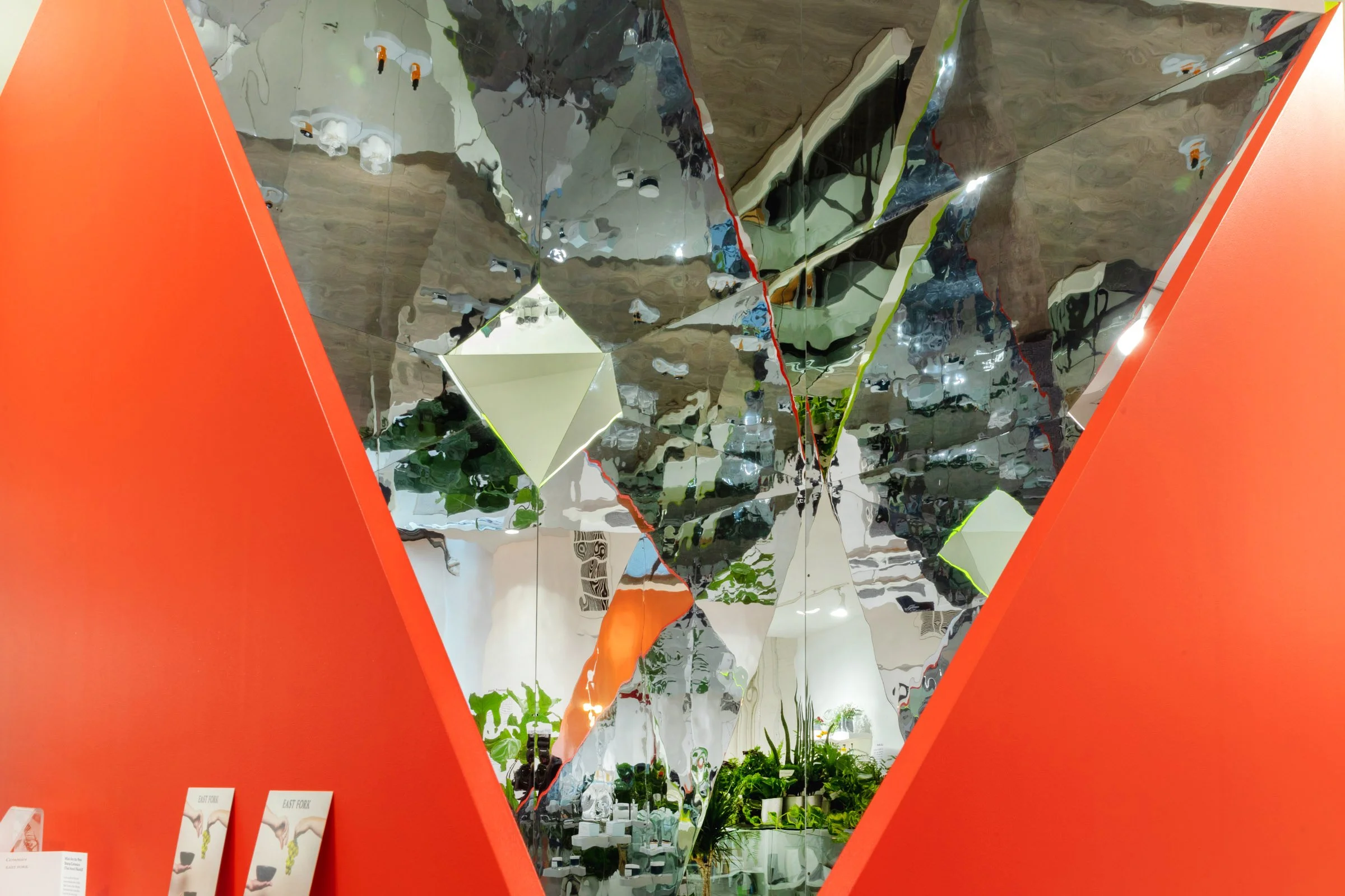 Geometric mirrored installation reflecting plants and a room with red walls.