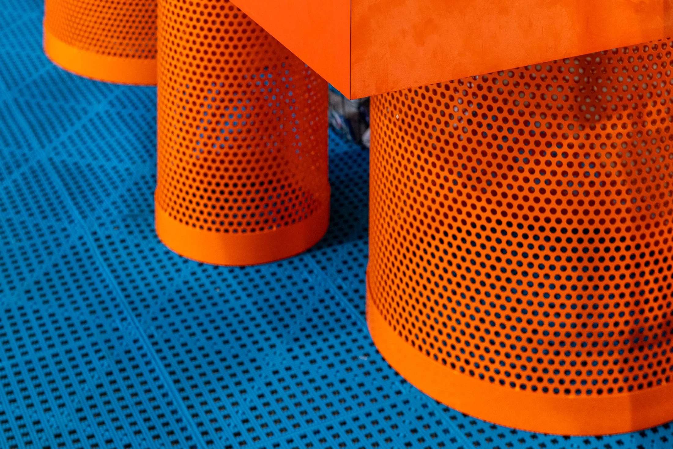 Close-up of orange perforated metal cylinders on a blue grid-patterned surface.