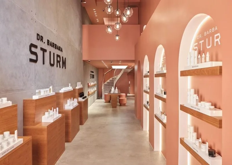 Interior of Dr. Barbara Sturm skincare store, featuring wooden shelves displaying beauty products and a modern design with peach-colored walls and spiral staircase.
