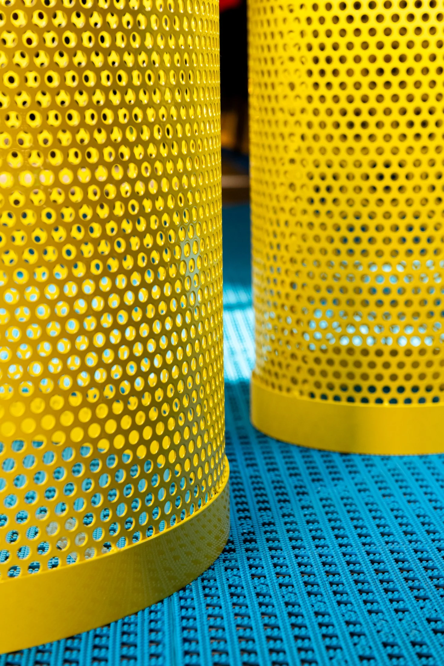 Close-up of two yellow perforated metal cylinders on a textured blue surface.