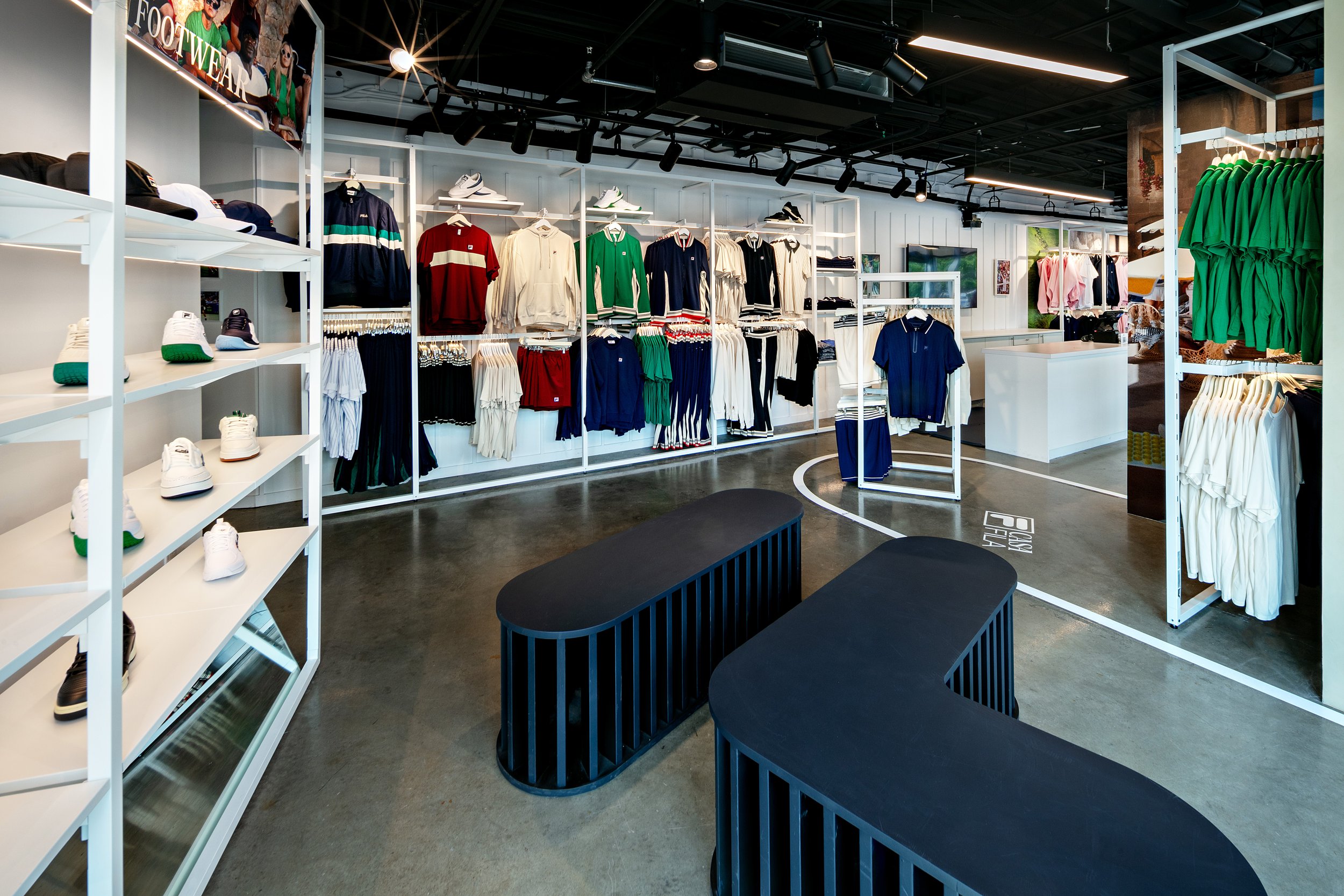 Retail store interior with shelves of colorful athletic apparel and sneakers displayed, featuring various clothing items such as shirts and jackets. Shop has a modern, open layout with bright lighting.