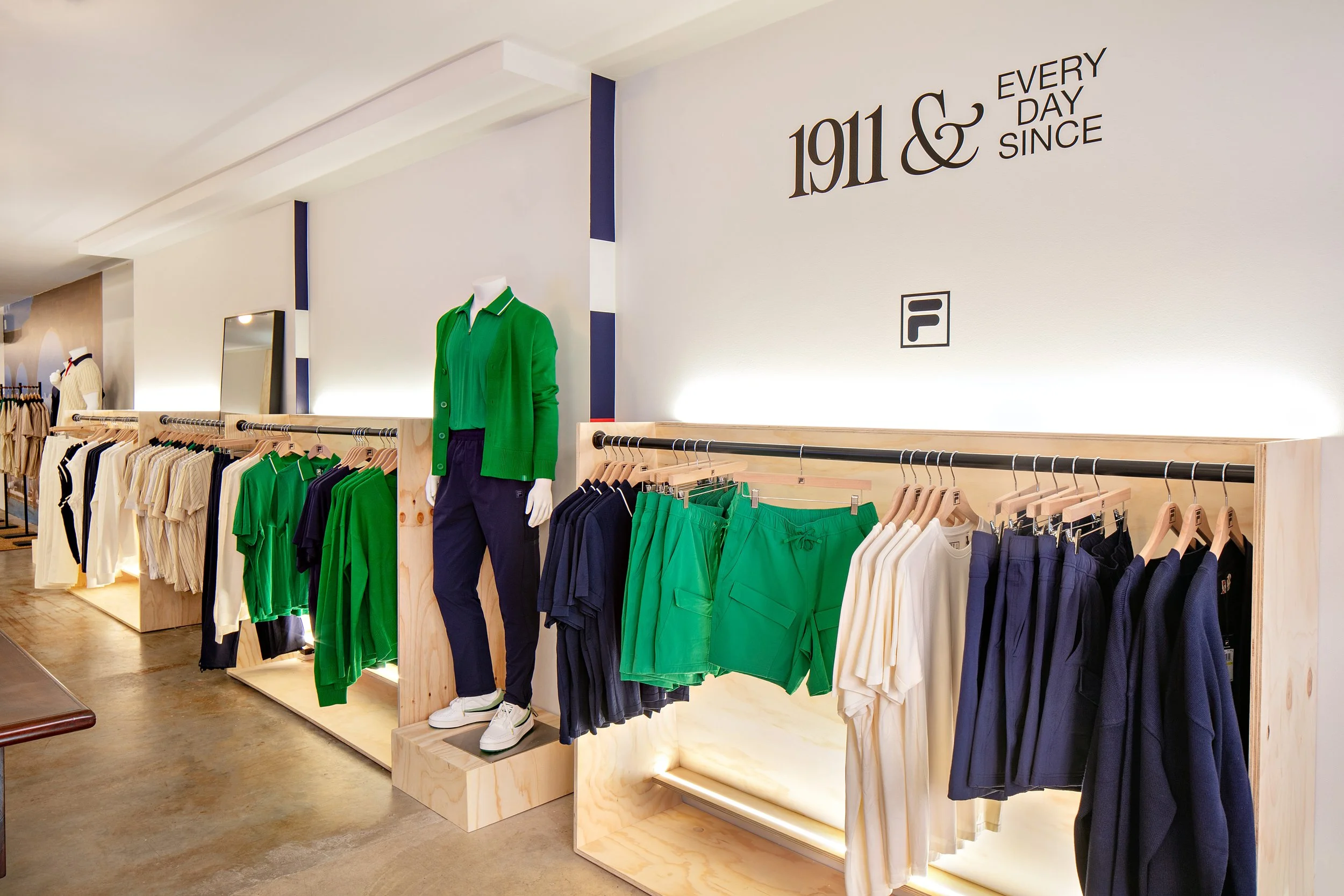 Clothing store interior with green, navy, and white outfits on display, featuring mannequins and clothing racks.