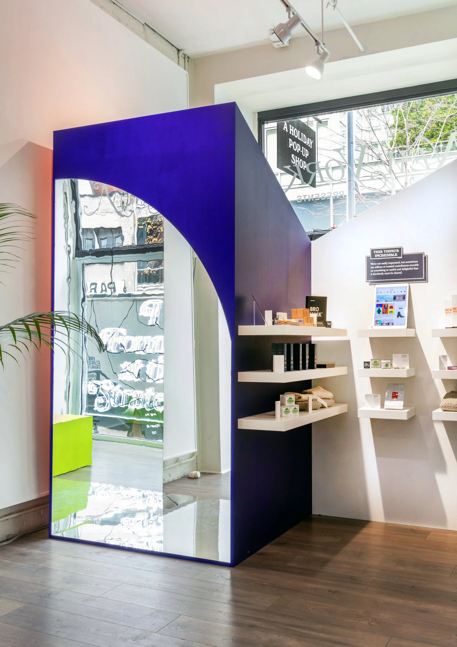 Interior of a modern pop-up shop with a blue and white color scheme, featuring a large mirror and shelves displaying various products.