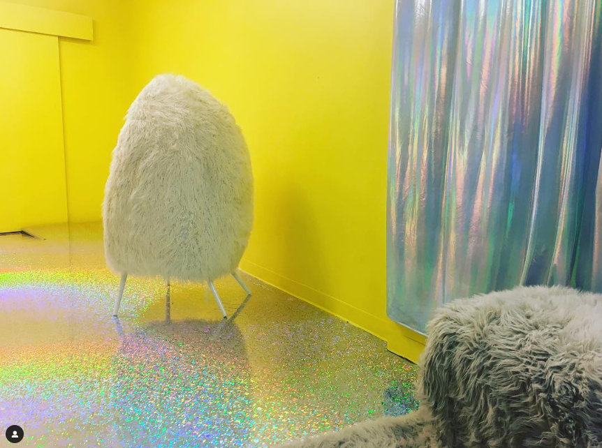 A yellow room with a fluffy white chair and a soft silver curtain, featuring a glittery floor.