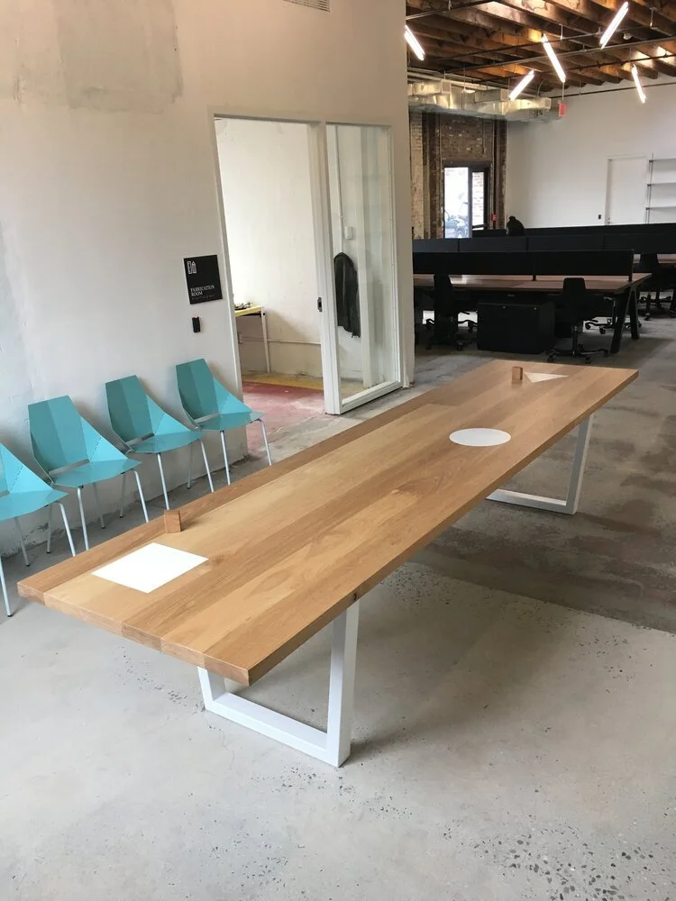 Modern office space with large wooden conference table, turquoise chairs, and exposed ceiling lights.