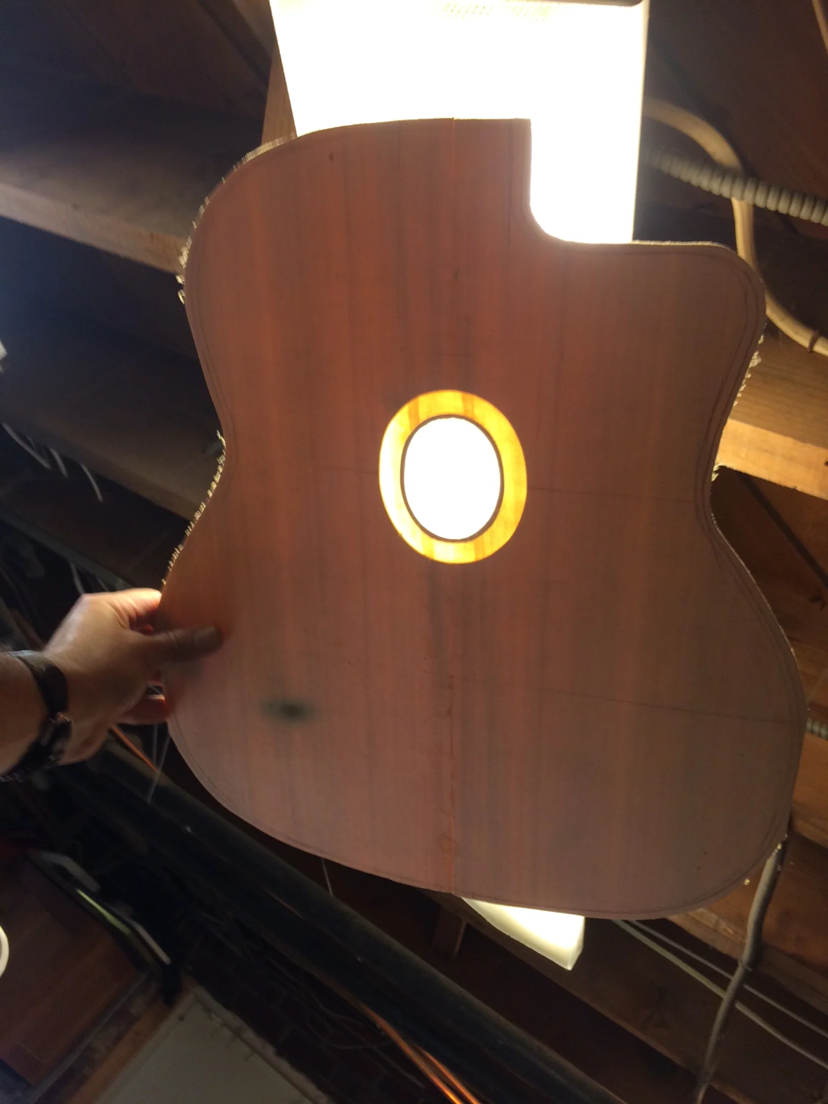 Here is a photo of the top. I used the bending box to bend the pliage but the heat lamp was a little too hot and actually charred the top. We are choosing to call that burn"character" and will blame it on a Gitanes cigarrette. The sound hole was routed out for the rosette. The remaining wood in the channel is extremely thin measuring about .75 mm thick. The seam joint down the center isn't perfect (as shown by the backlight) but I hope that the reinforcing veneer on the back together with the heel and neck block will keep it all together.