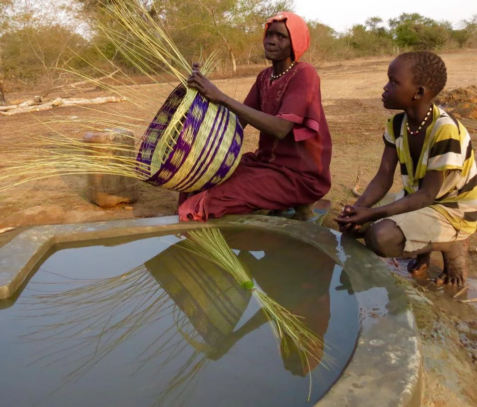 Achan soaks the reeds needed for her basket. with a well nearby she will now have time to make and sell baskets, and her daughter can attend school.