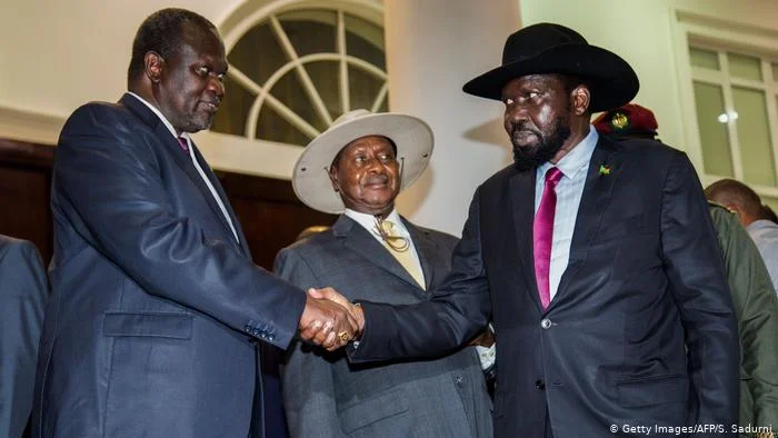 President Salva Kiir (right) and opposition leader Riek Machar (left) shake hands while Ugandan President Yoweri Museveni looks on.