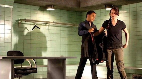 Cinna (Lenny Kravitz) helps Katniss on with her jacket in The Hunger Games . 