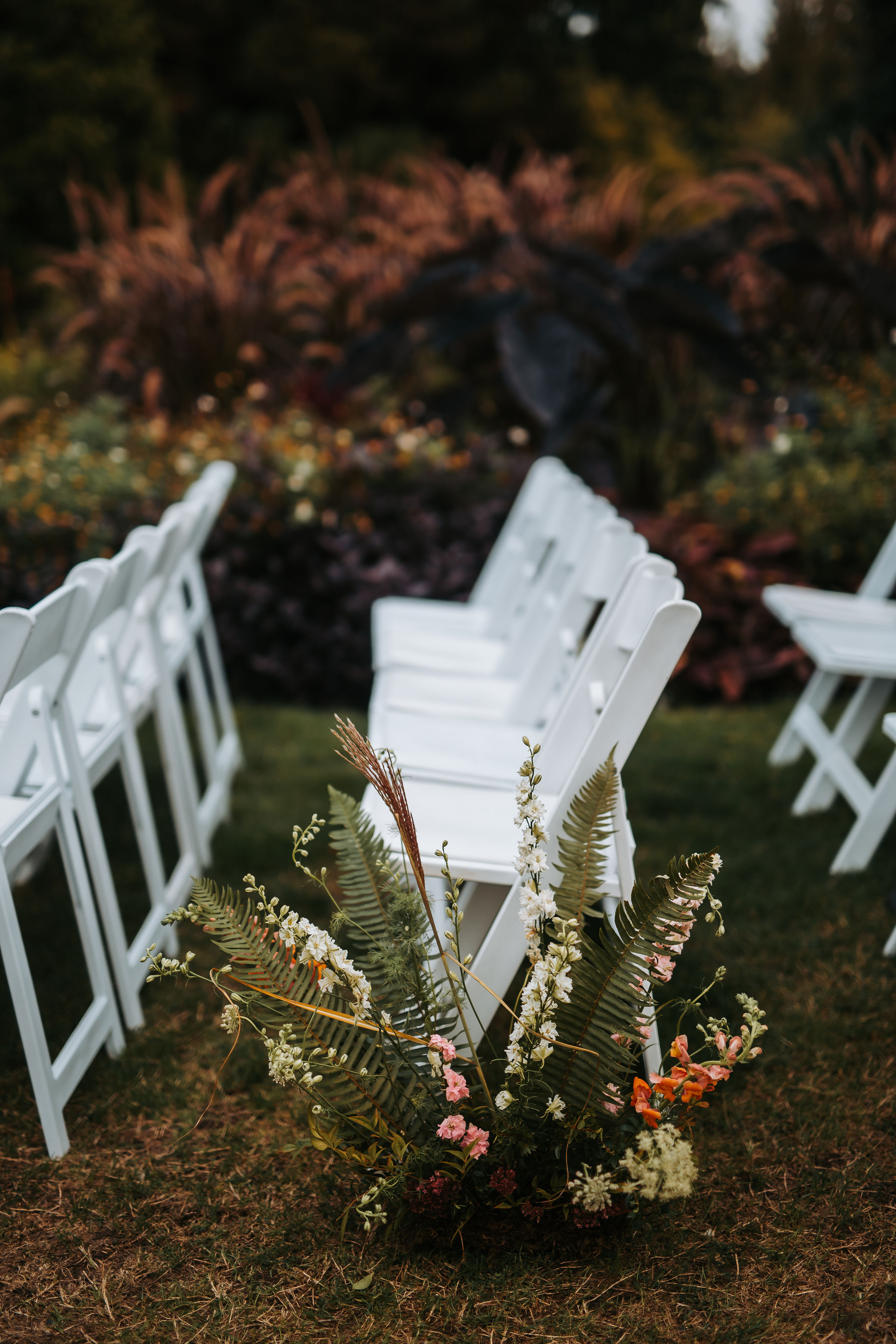 Flowers and Greenery sprout up from the ground to decorate the ceremony aisle at Stanley Park Pavilion. White folding garden chairs | Keepsake Events