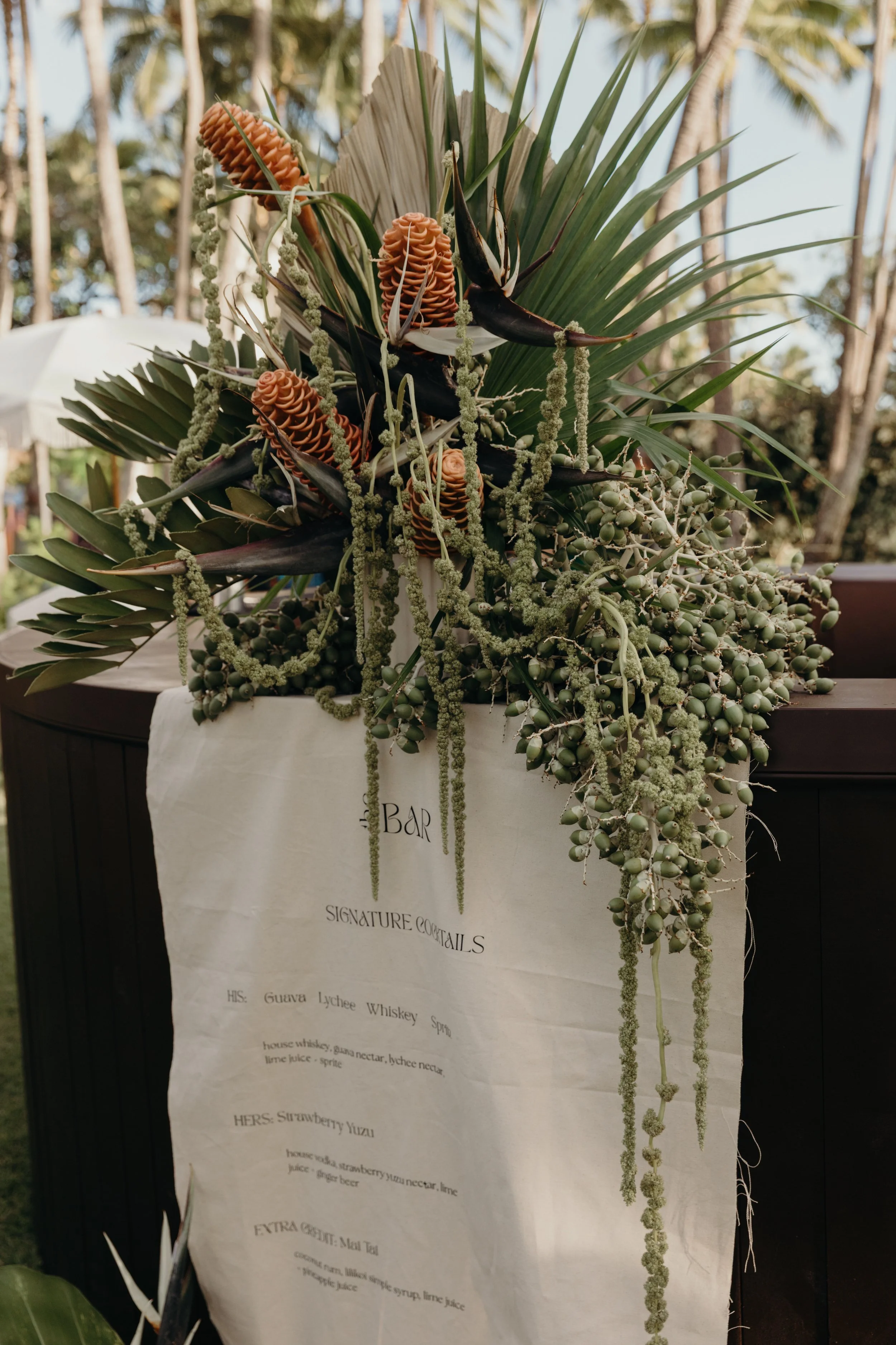 A floral arrangement with green palm leaves, beehive ginger flowers, set against a background of palms by florist Mei Day.