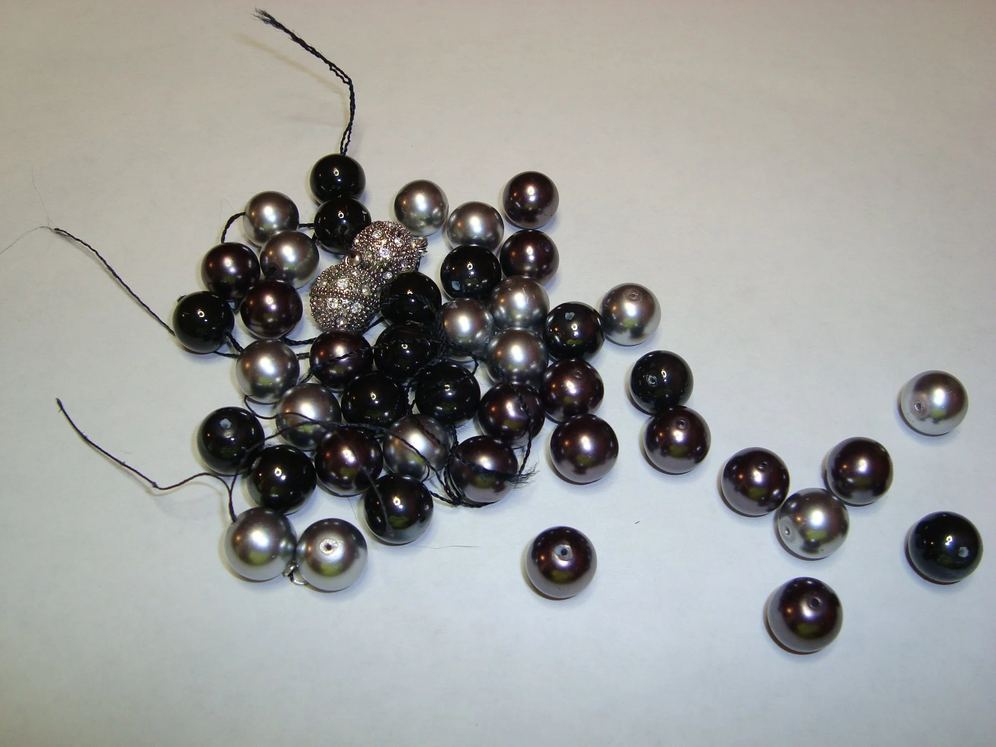 A collection of black, silver, and decorative beaded necklaces and loose beads on a white surface.