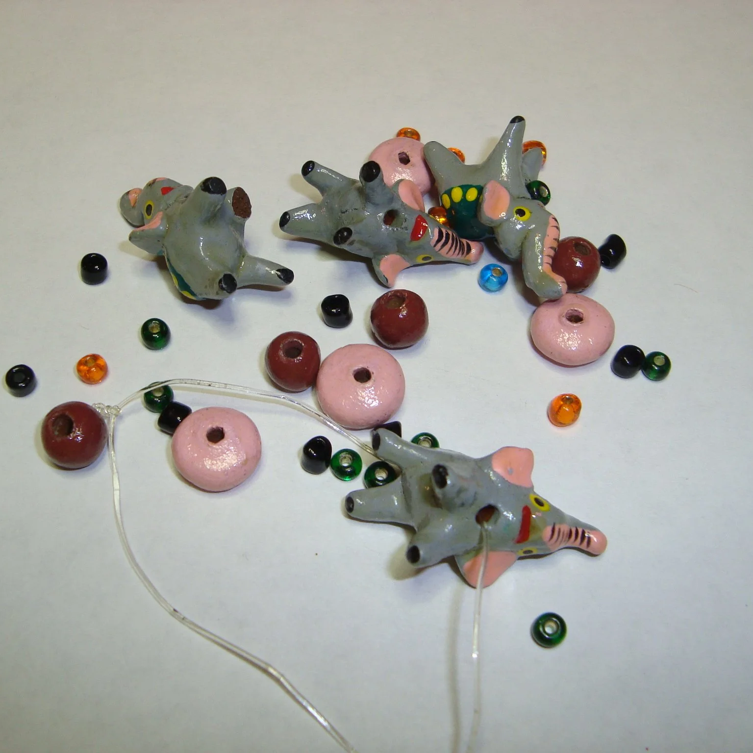 Colorful glass animal figurines resembling frogs or lizards, small beads, and donut-shaped objects scattered on a white surface.