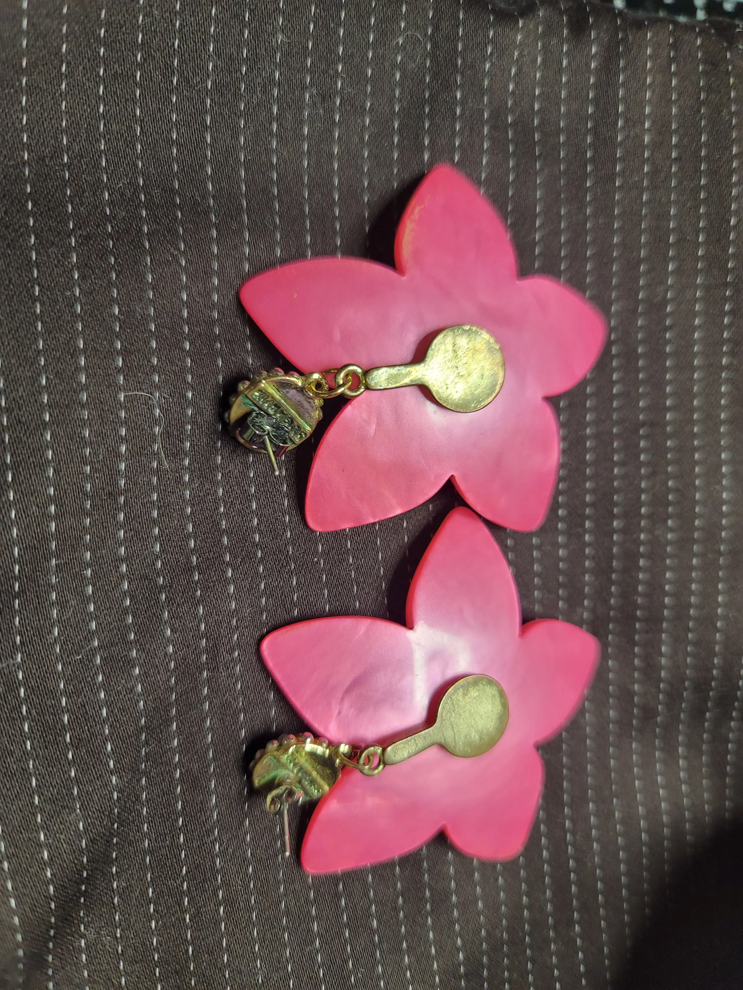 Pair of pink flower-shaped earrings with gold-colored backings and hooks placed on a textured dark surface.