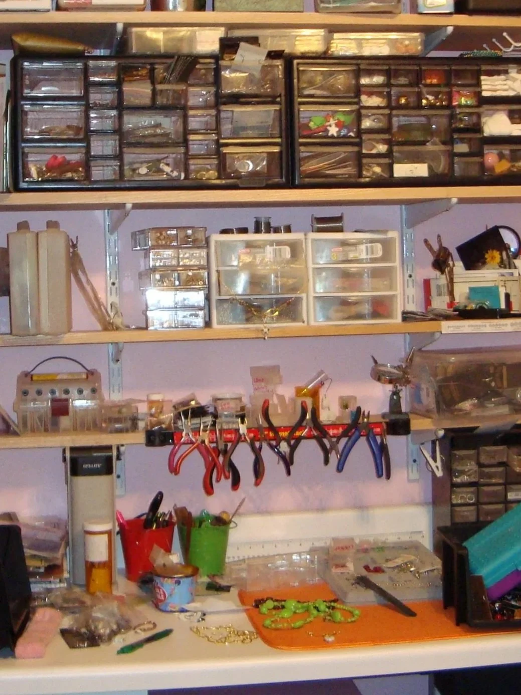 Workstation with jewelry-making supplies, tools, and organized containers on shelves and a table.