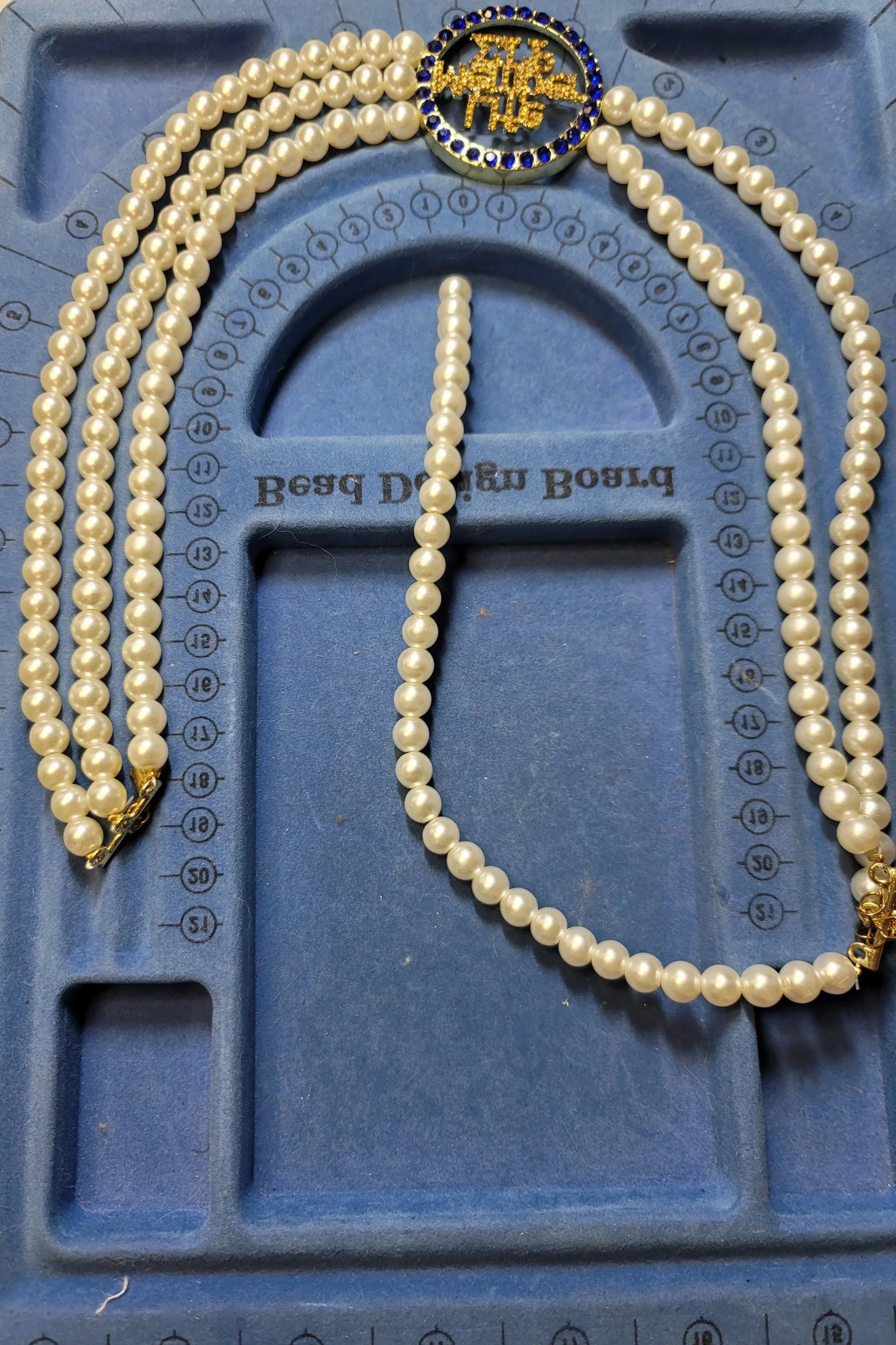 A blue jewelry box tray with a pearl necklace and a decorative pin with the word 'WILD' on it.