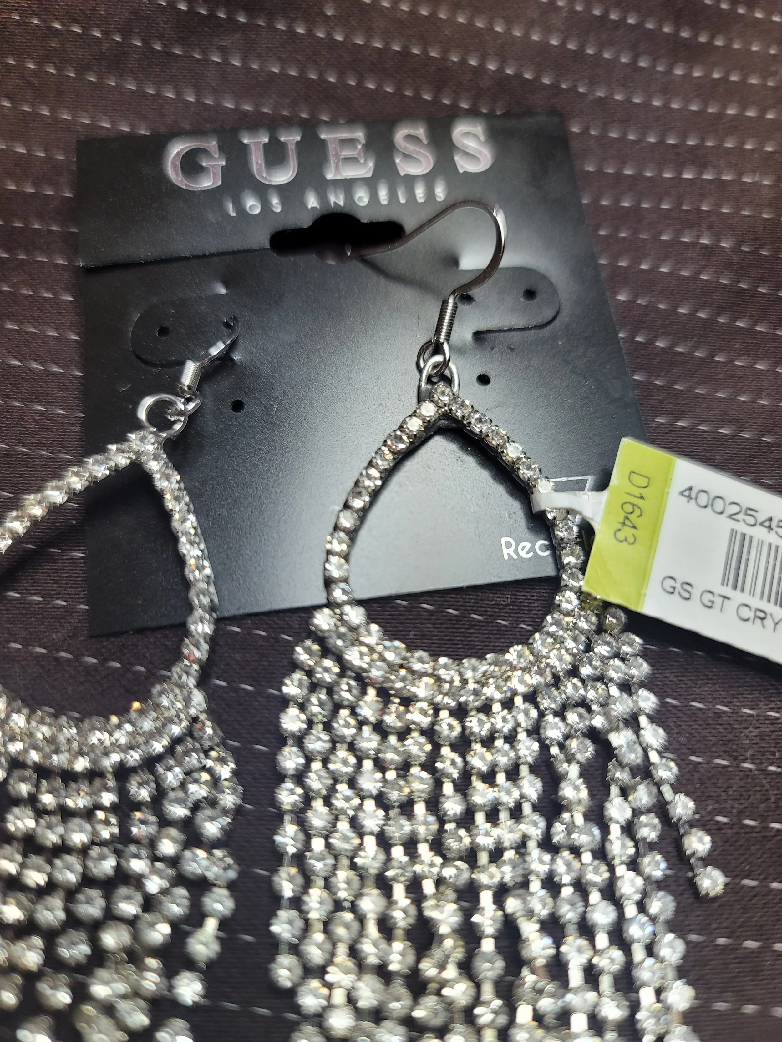 Pair of sparkling rhinestone earrings with teardrop shape, hanging on Guess brand display card.
