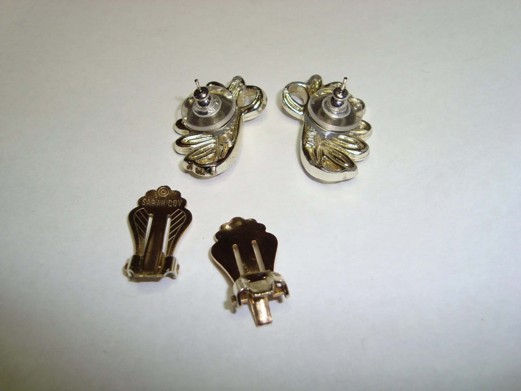 Pair of silver earrings shaped like leaves, and two hair clips, one with 'Sarah Cody' engraved on it, on a white surface.