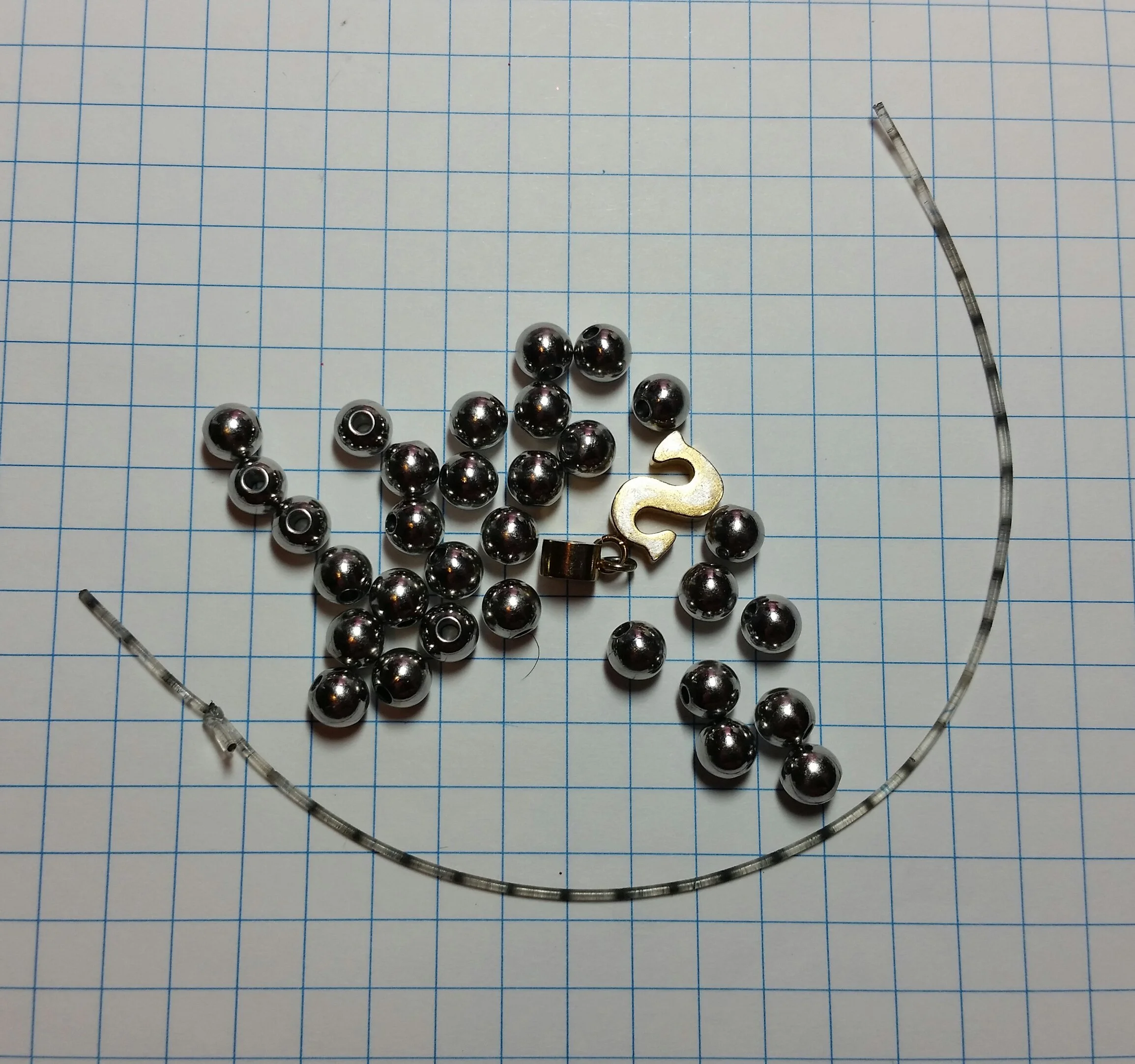 Scattered metallic beads, a small gold-colored '2' charm, and a black number '2' charm on a piece of graph paper with blue grid lines.