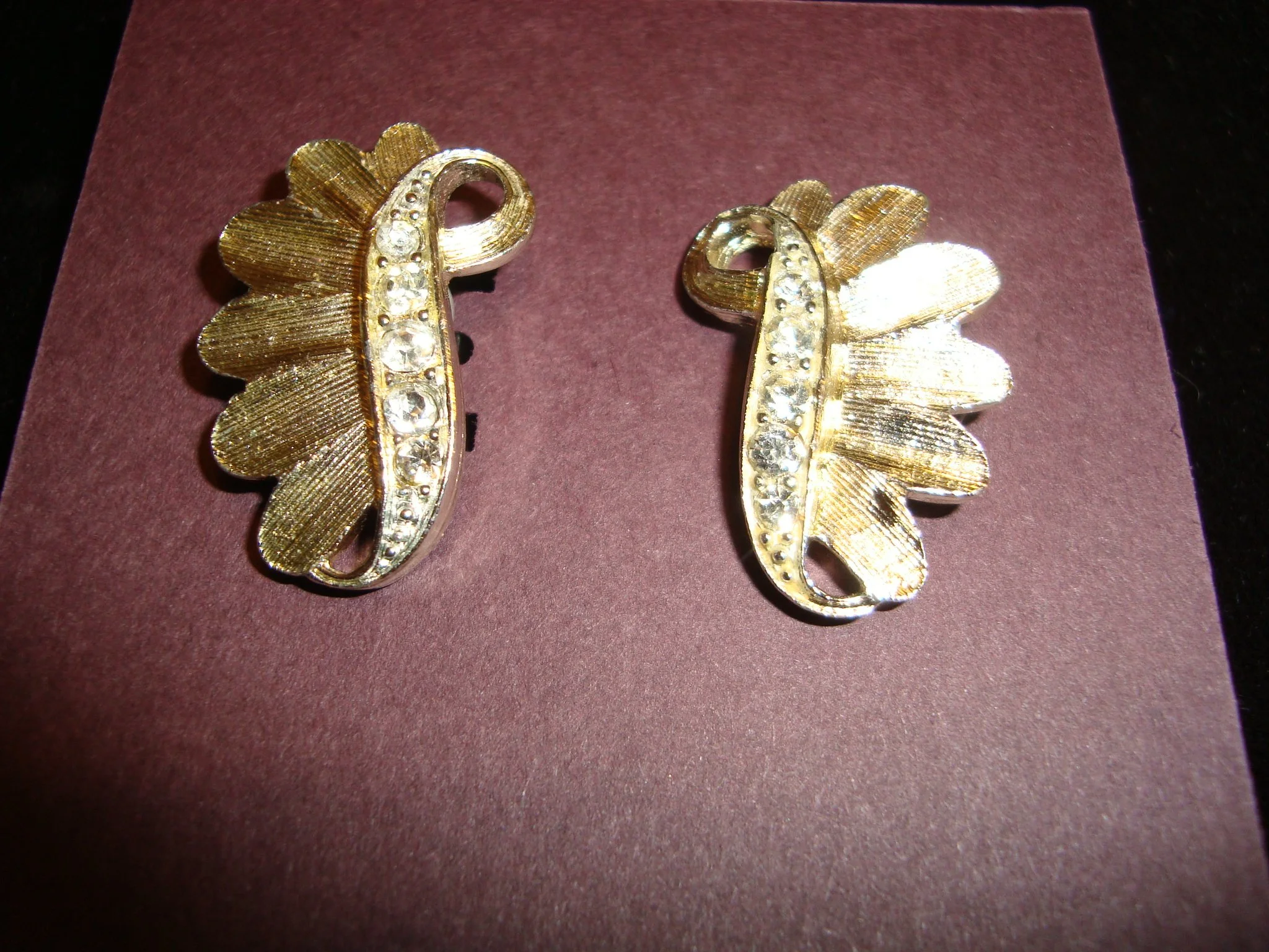 Pair of gold earrings shaped like wings with small clear gemstones in the center, displayed on a purple surface.
