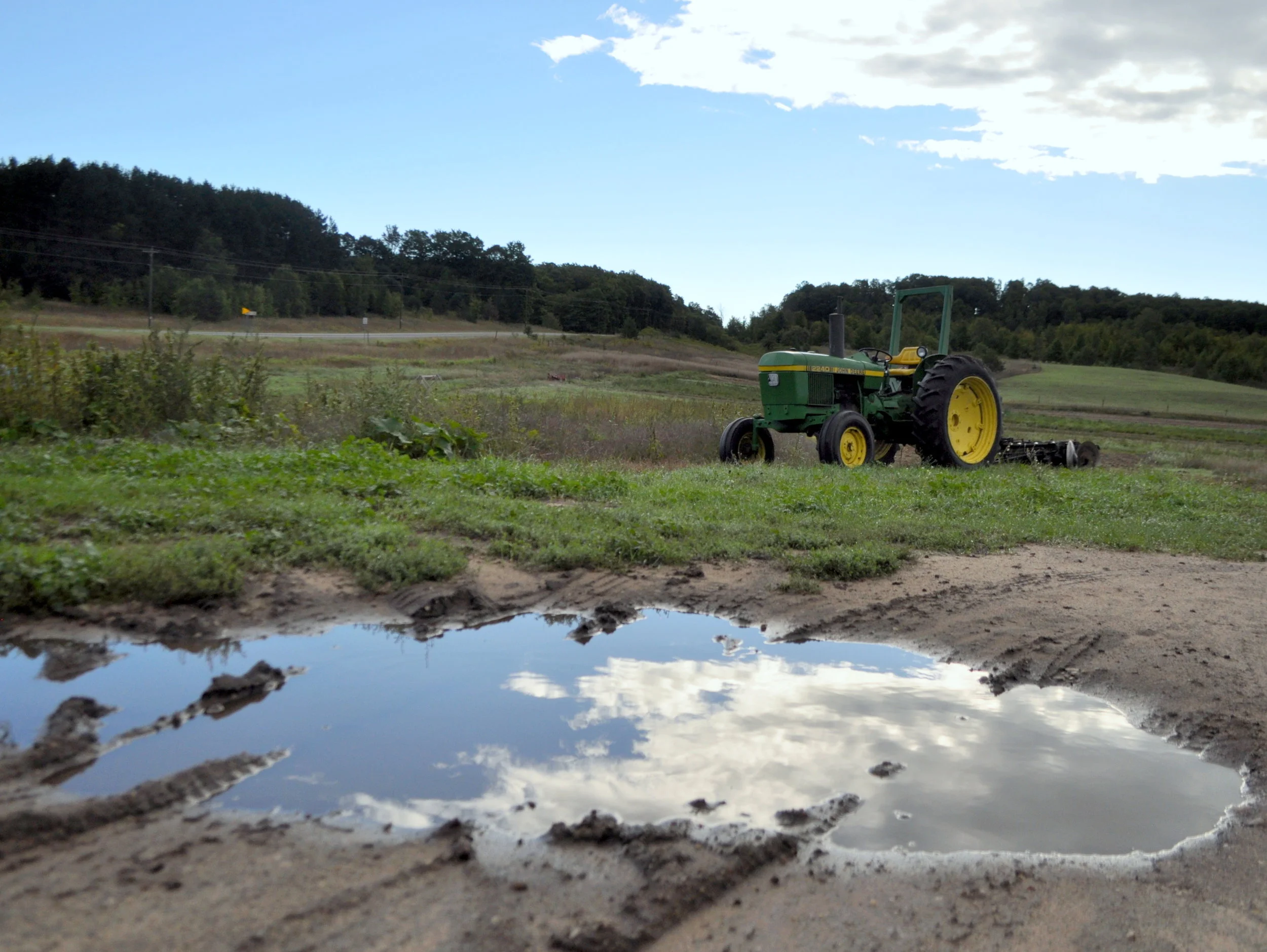 A puddle reflects the sky and a tractor takes five.
