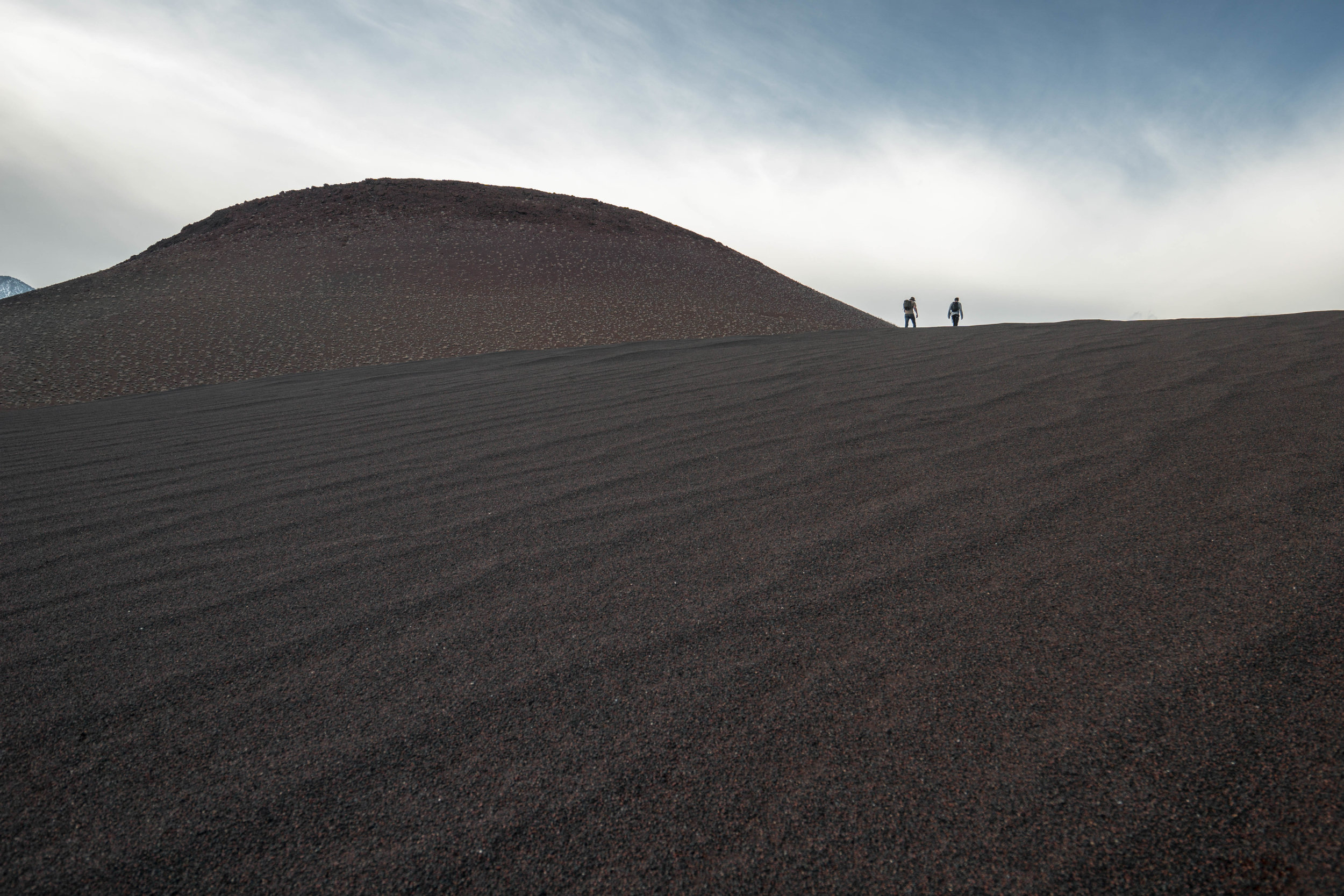 The wind-swept sand dunes shift from a scarlet red to a mystifying blackened hue.