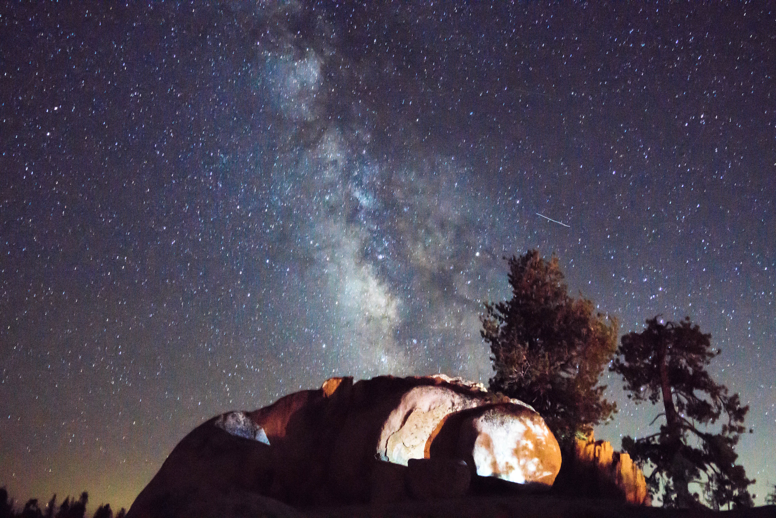 The Milky Way dances across the sky as the fire lights up some nearby boulders.