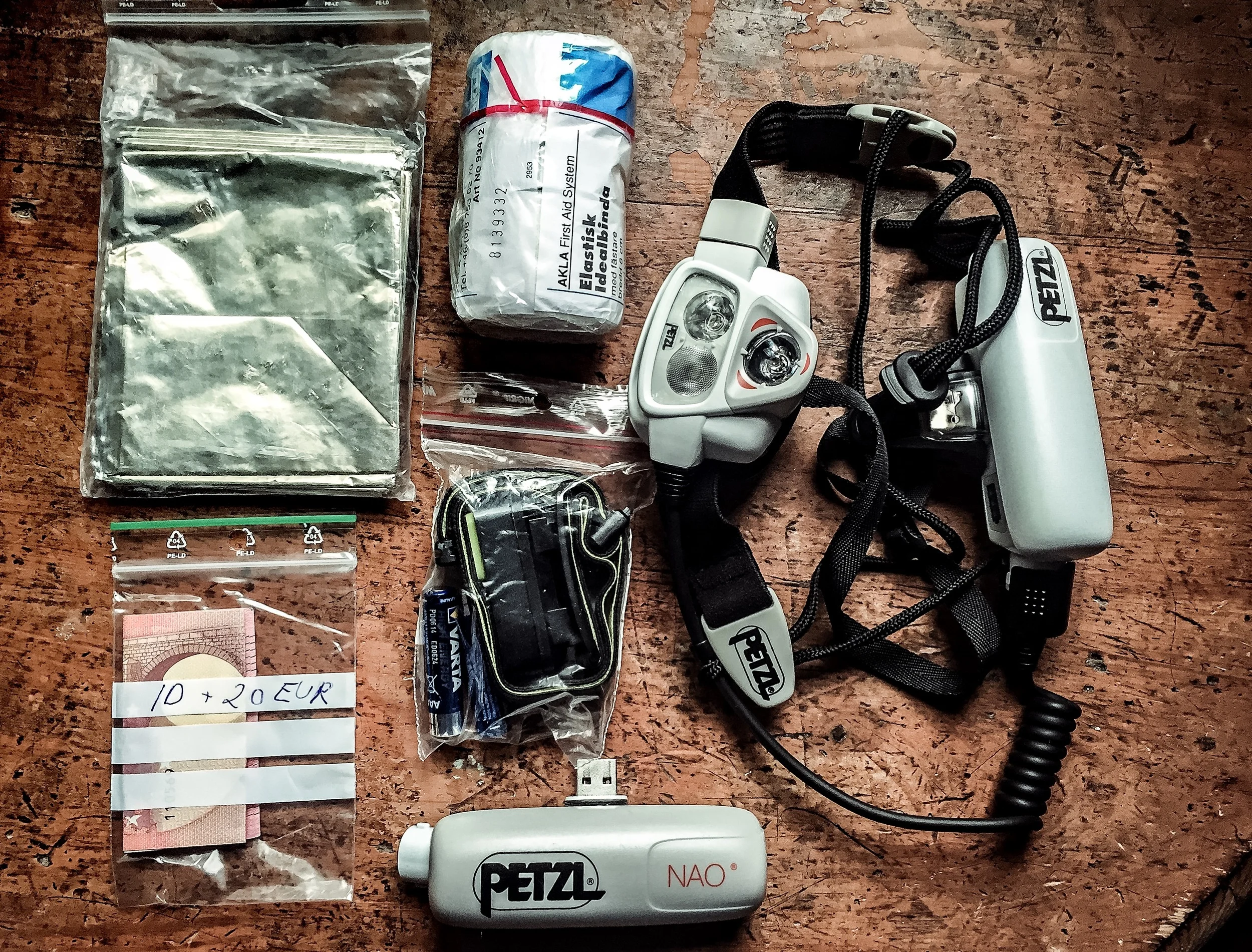 Räddningsfilt, elastisk binda, 20 EUR, lilla pannlampan ION från Black Diamond plus extrabatterier till denna, stora pannlampan Petzl NAO plus extrabatteri till den. Saknas på denna bild: mobiltelefon och ID-kort (ska sen ligga i samma påse som de 20 EUR man måste ha med sig).