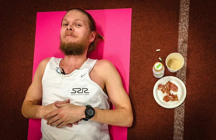 Henrik Roos tar en paus under 24-timmarsloppet på Personliga Rekordens Tävling 2017. Han fikar på bacon, fett-kaffe, saltkapslar och BCCA-kapslar.