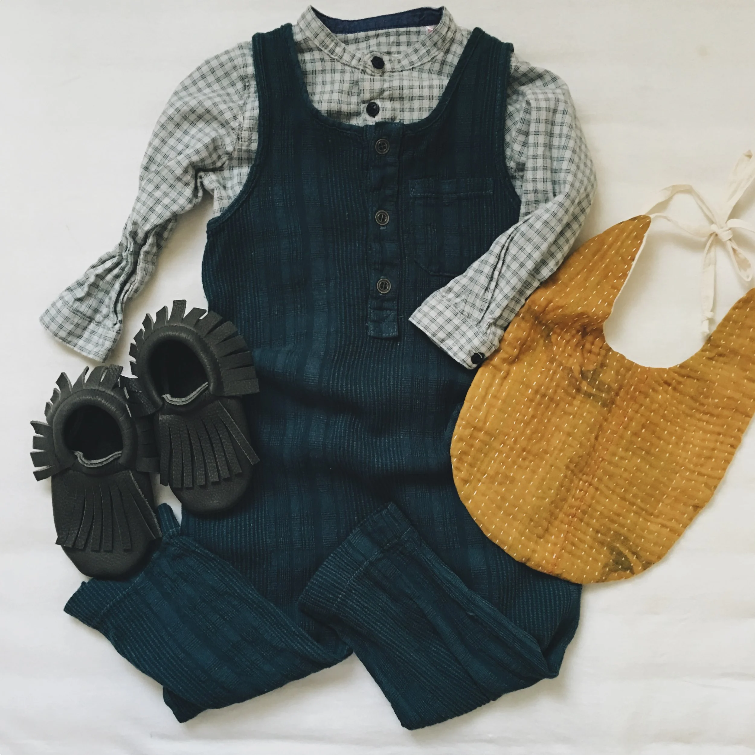 Romper - Nico Nico Clothing c/o Murray & Finn ; Plaid Shirt - Zara ; Bib - Wild Winnie ; Raven Moccasins c/o Little Pine Outfitters