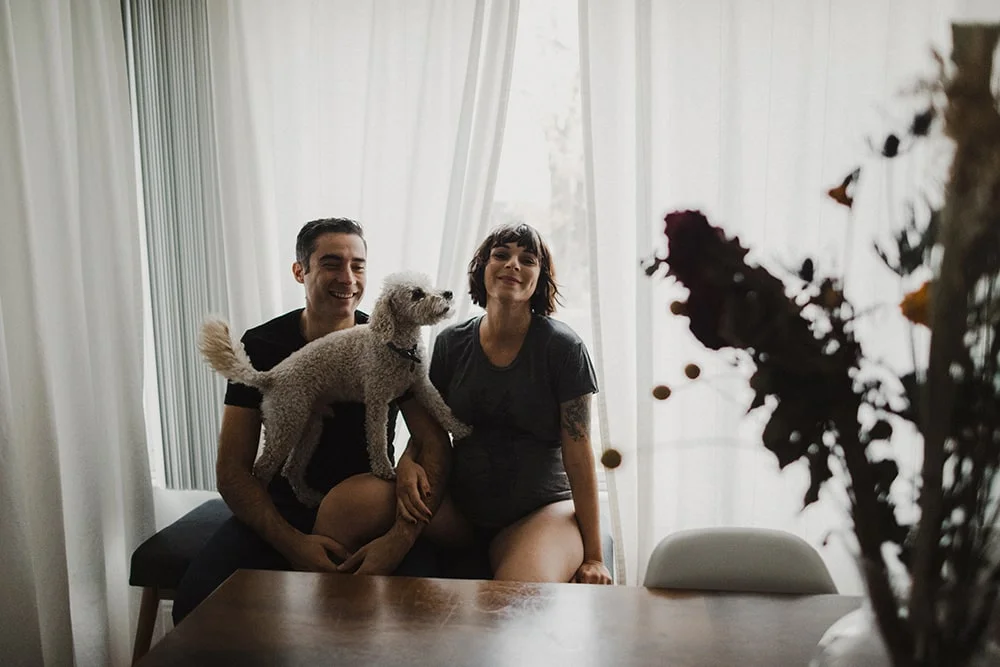 couple laughing and playing with dog next to window