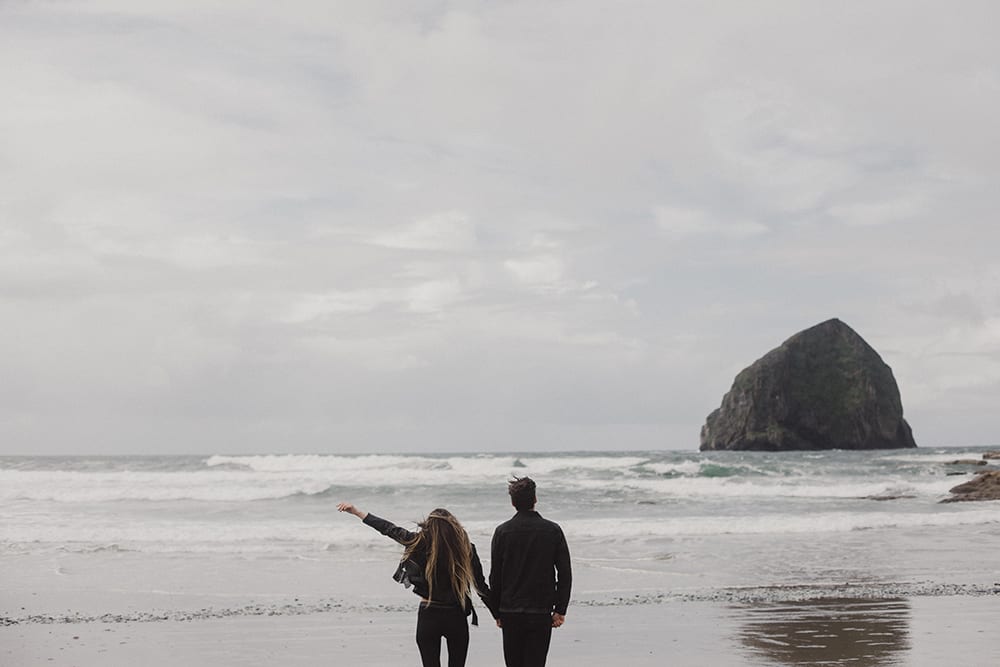 Couple walking toward water, girl throwing hand in the air at cape kiwanda