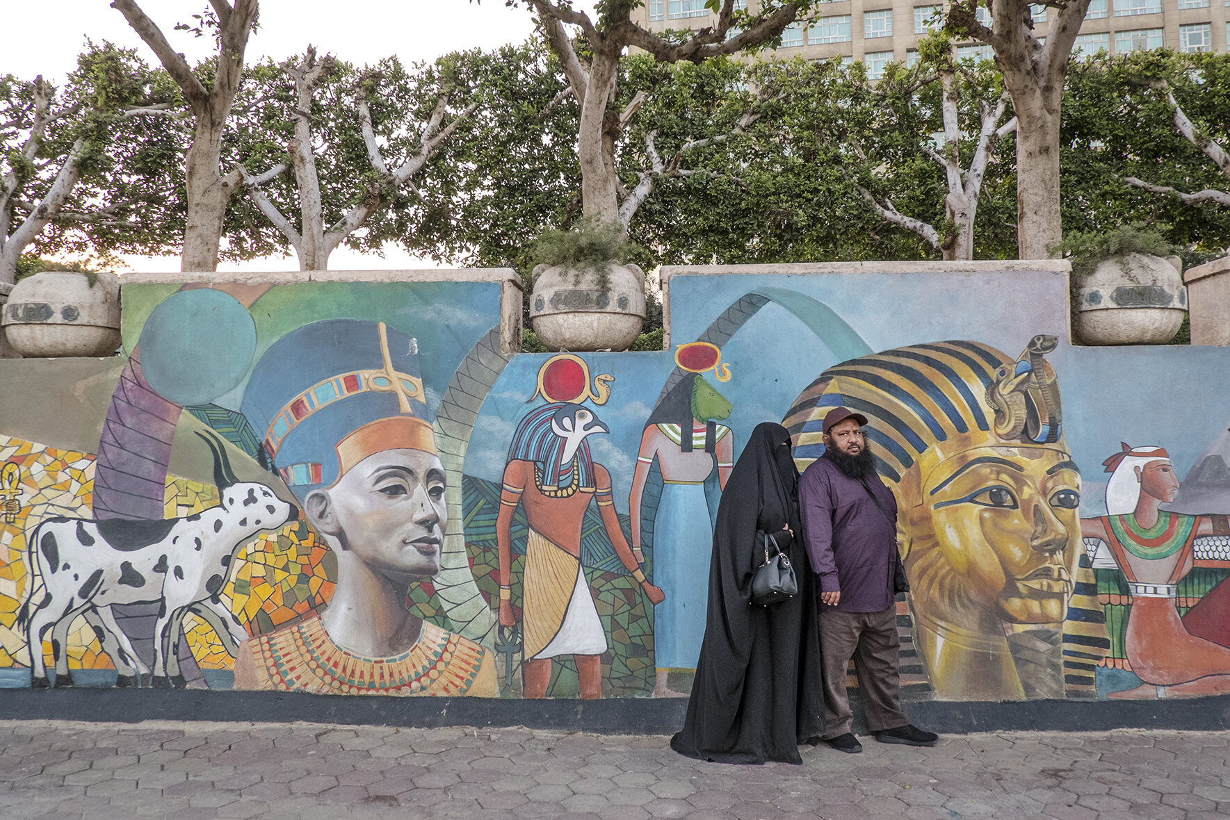 A religious Egyptian couple posing in front of a street paining in Cairo park located close to Tahrir square and Kasr Al Nile Bridge, where revolution against the previous regime started in 2011. During the year that followed, the Muslim Brotherhood, party which came to power, did everything they could to prevent gender equality and bring back the deep islamisation of the country.Among other plans their political agenda included: lowering the minimum age for marriage from 18 to 12, abolishing women's right to divorce and decriminalizing the practice of female genital mutilation.After Abdel Fattah El-Sisi become president some of those laws were changed but the budget for sexual education and family planning was lowered and several collaborations with international organisations were suspended. December 2018, Cairo, Egypt