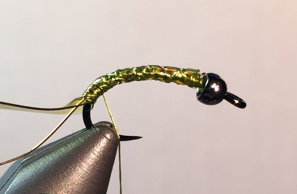 Step 2: Tie in a 2” section of fine copper wire, followed by a 1-1/2” section of olive Body Glass. Tie both the entire length of the shaft, up to the bead to build up the body.