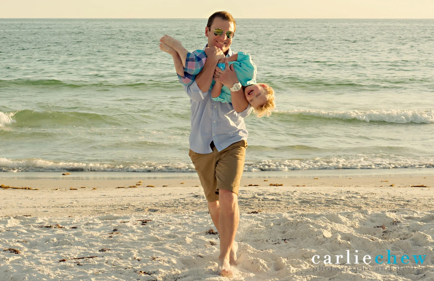 Father running with son in arms while being photographed by Carlie Chew Photography on Anna Maria Island. 