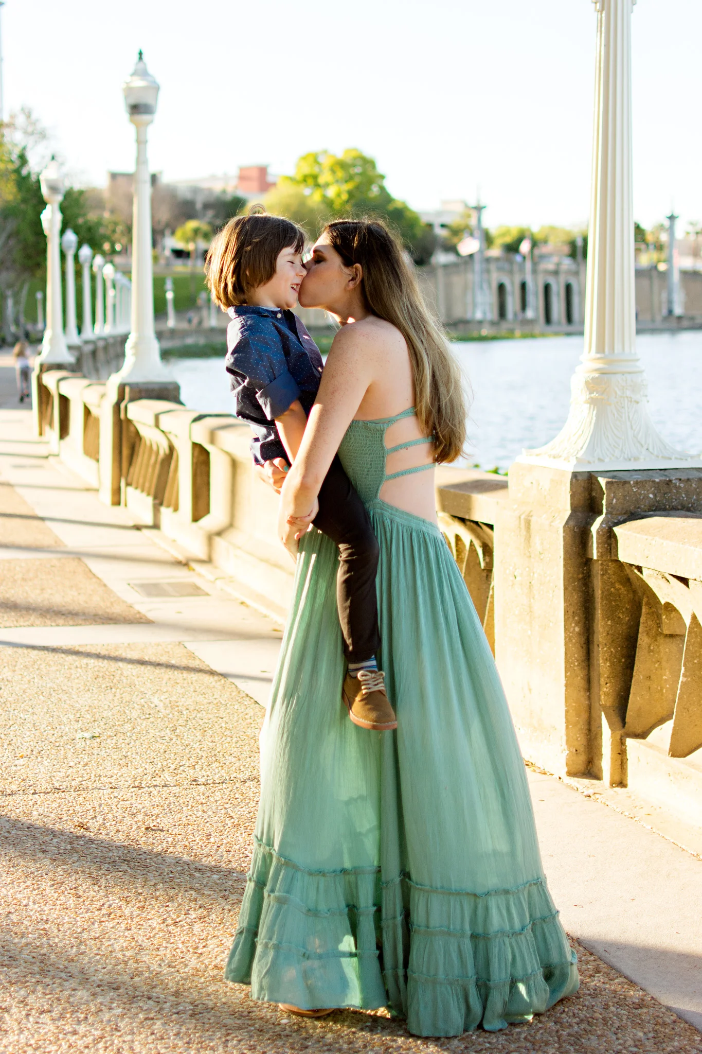 Pregnant mother hold son on her belly and kisses him at Mirror Lake, Lakeland FL with Carlie Chew Photography 