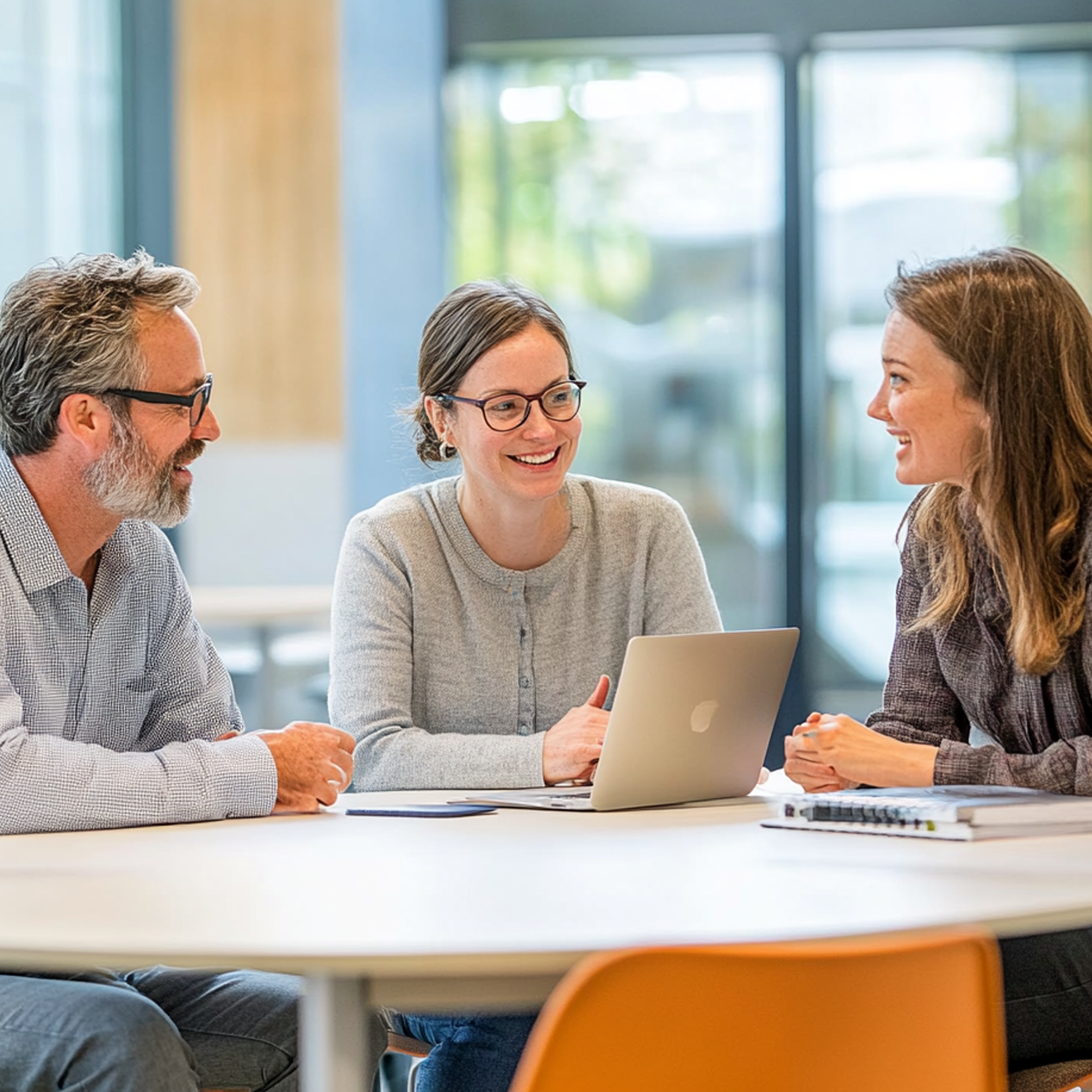 Four adults sitting around a table, smiling and having a discussion in a bright, modern office with large windows.