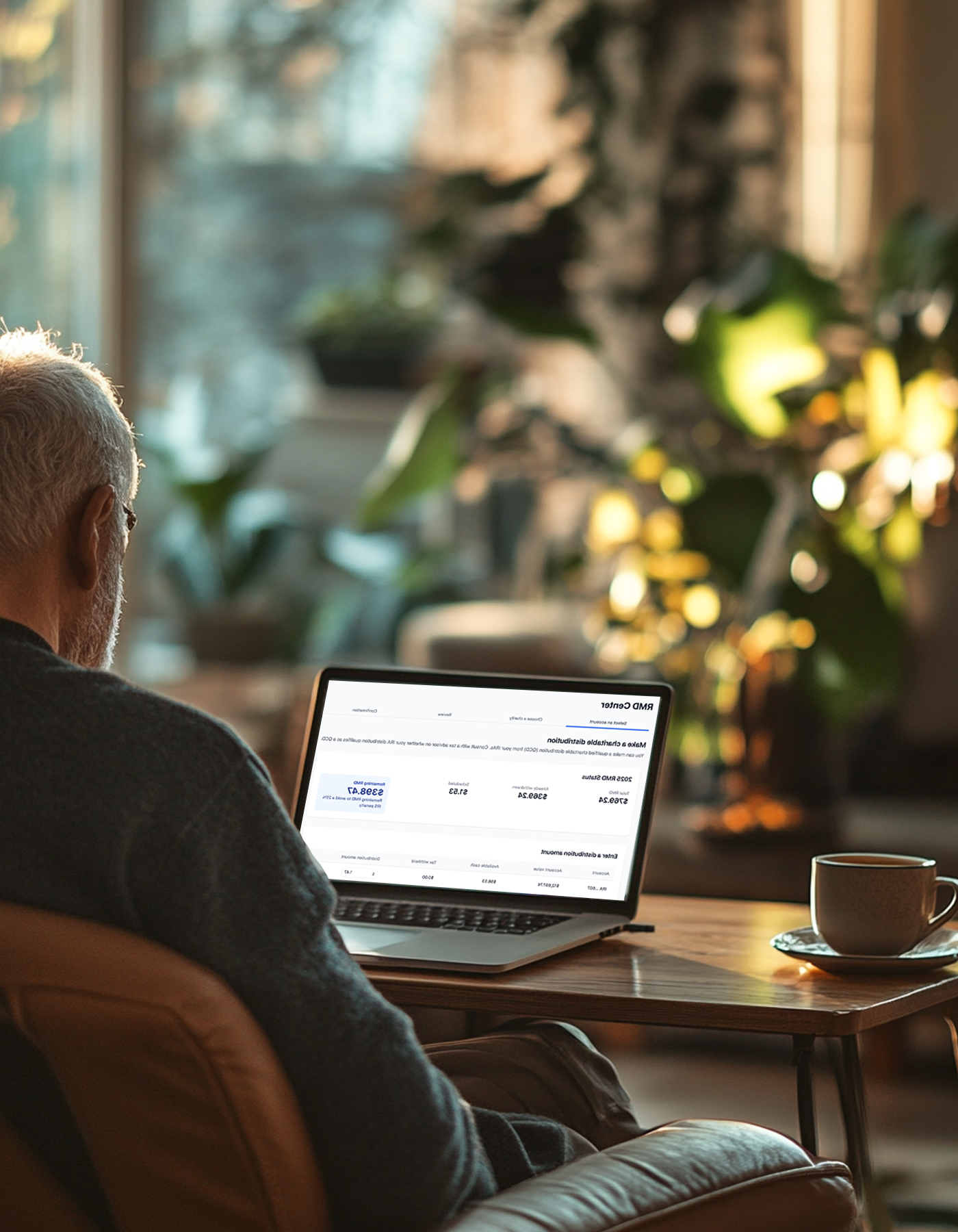 An older man with gray hair sitting at a wooden table, using a laptop in a cozy room with sunlight streaming through a window, with potted plants and warm decor in the background.