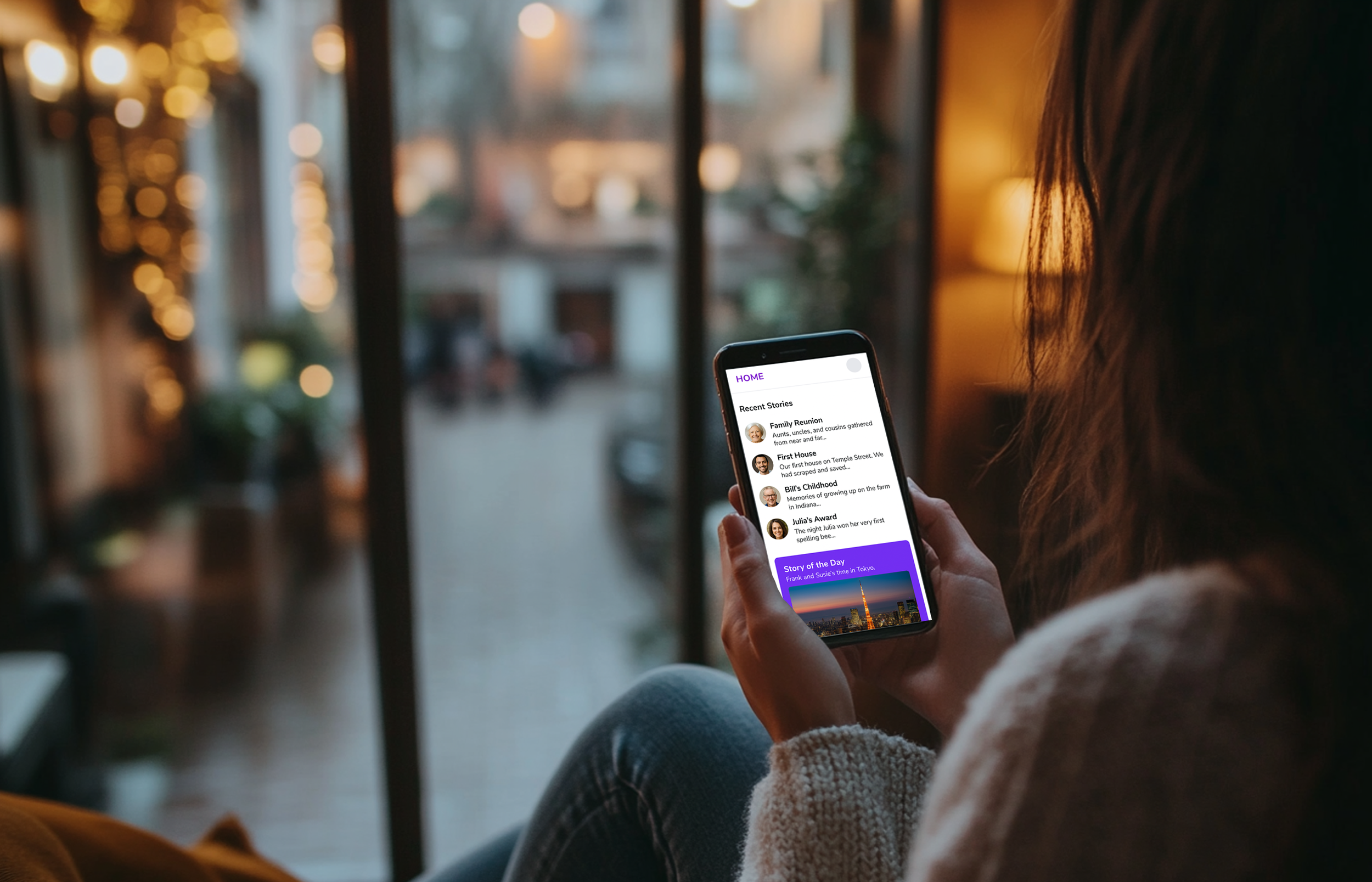 Person holding a smartphone in a cozy indoor setting with blurred warm lights and window in the background.