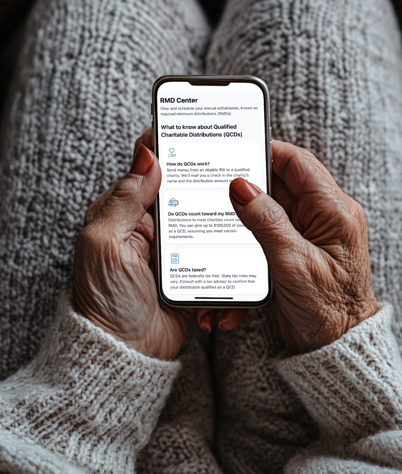 Close-up of elderly person's hands holding a smartphone with a financial app open, showing information about charitable distributions (QCDs).