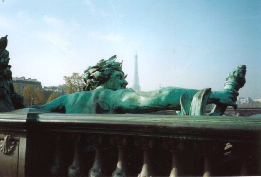 Paris Bridge: A graceful sculpture adorns the Alexander III Bridge, with a whisper of the Eiffel Tower in the background. The scene captures the city’s iconic blend of art, architecture, and timeless charm.