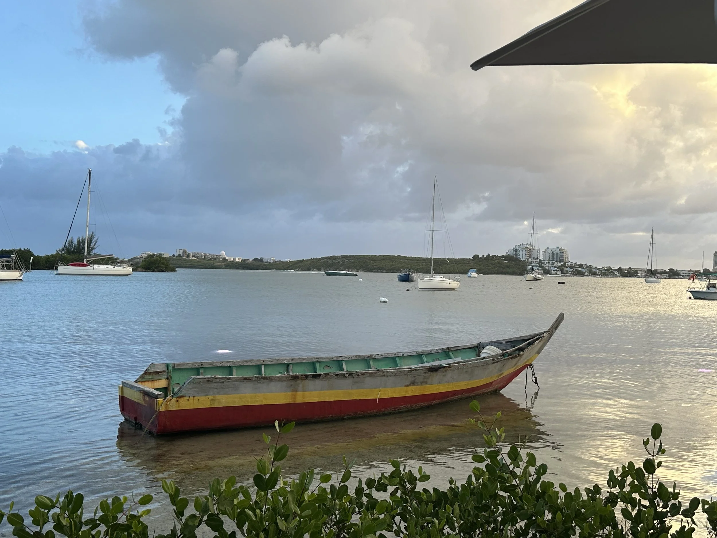 Peaceful Boat: A boat rests quietly near the shore of a restaurant along the coast of St. Maarten, gently rocking with the tide. Mirroring a day untouched by urgency, invoking calm, stillness, ease, and the natural flow of life.