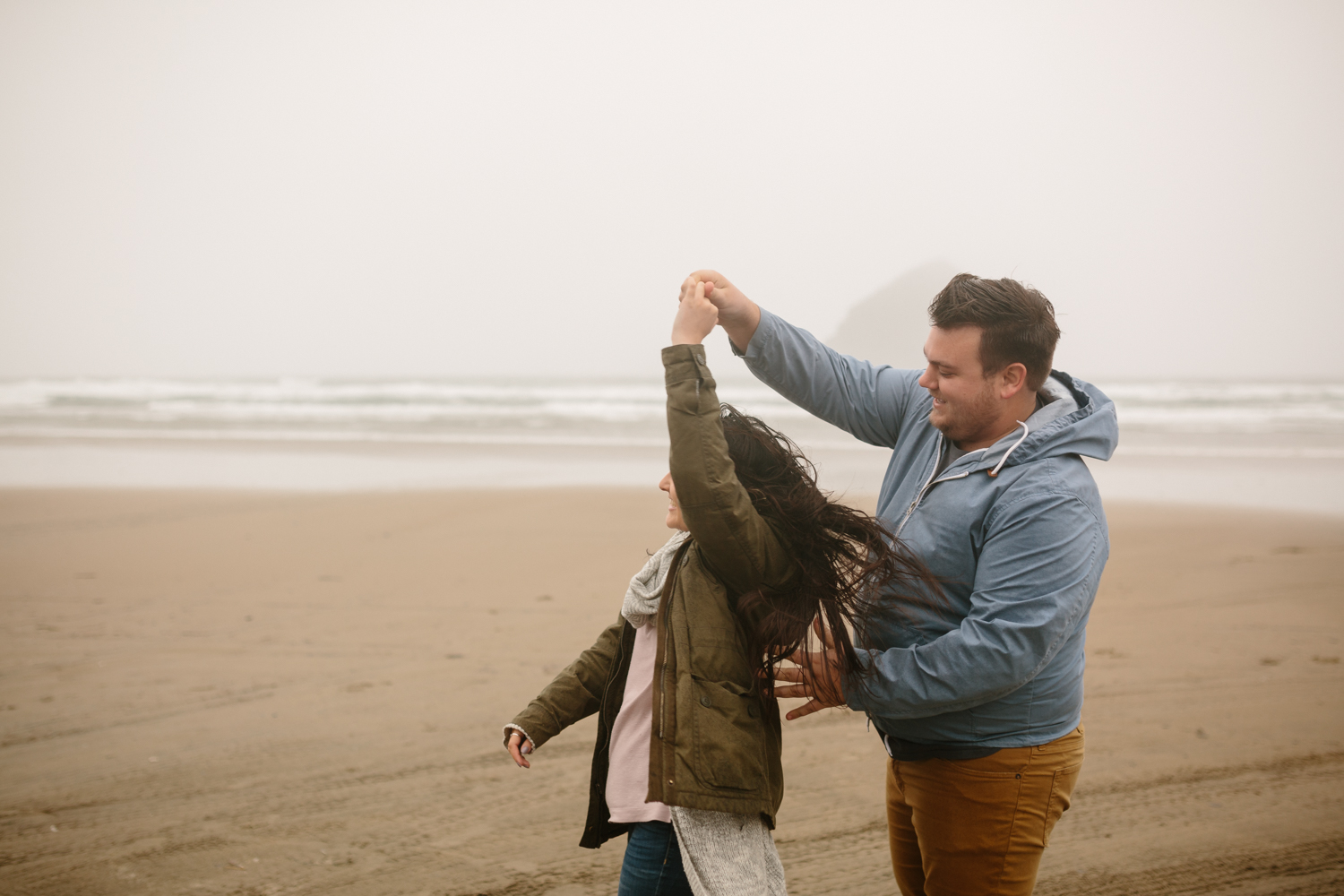 Happy young couple dancing on the beach in the wind and cold