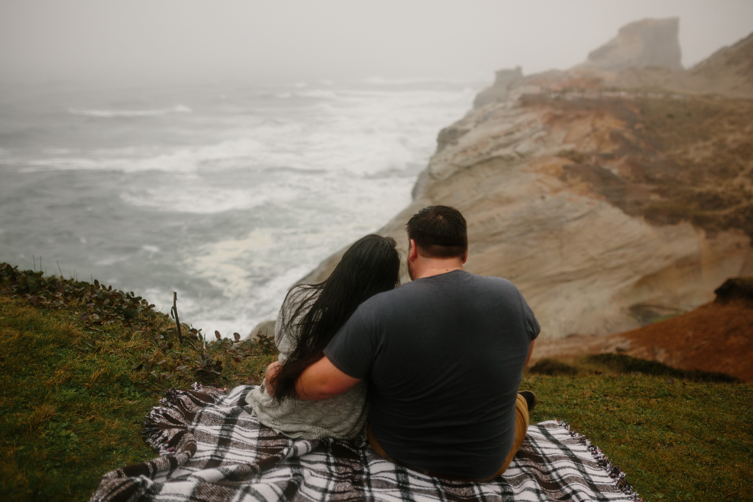 A young couple sitting on a cliff overlooking the ocean on the O